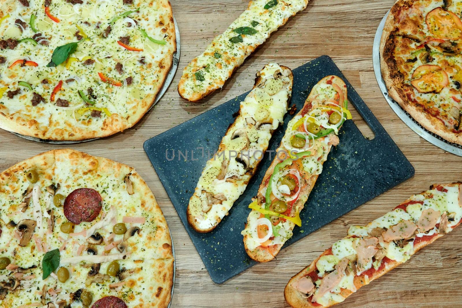 A variety of pizzas and breadsticks are displayed on a table. The pizzas are of different sizes and flavors, while the breadsticks are cut into smaller pieces