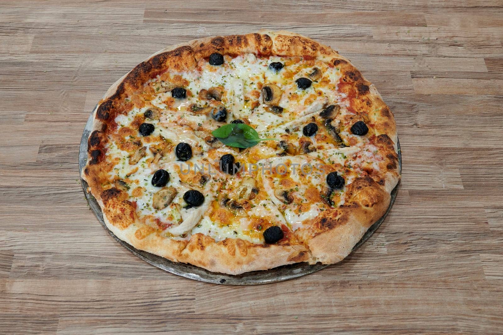 A pizza with olives and mushrooms on it. The pizza is sitting on a wooden table. The pizza is ready to be eaten