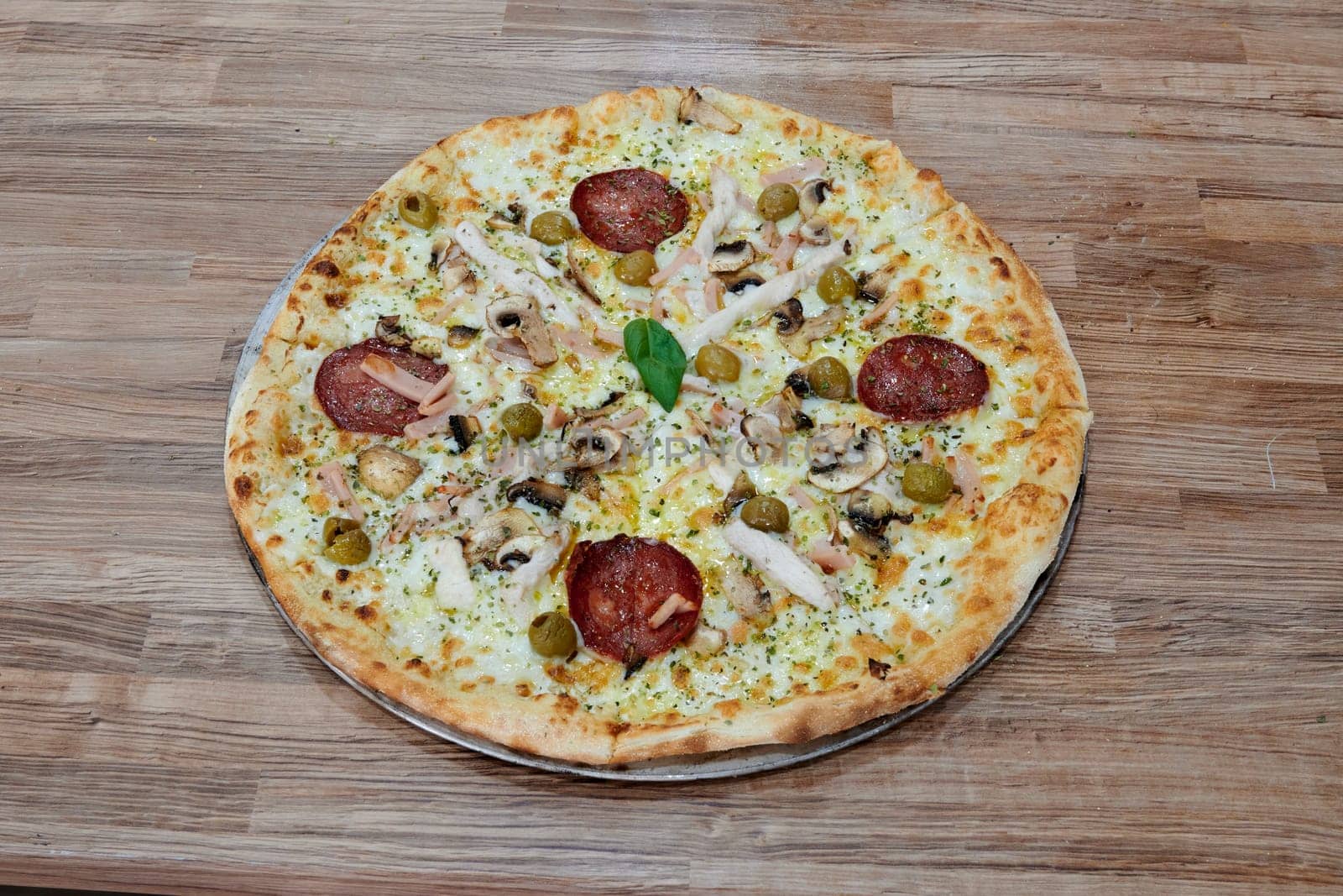 A pizza with a variety of toppings including chicken, olives, and mushrooms. The pizza is sitting on a wooden table