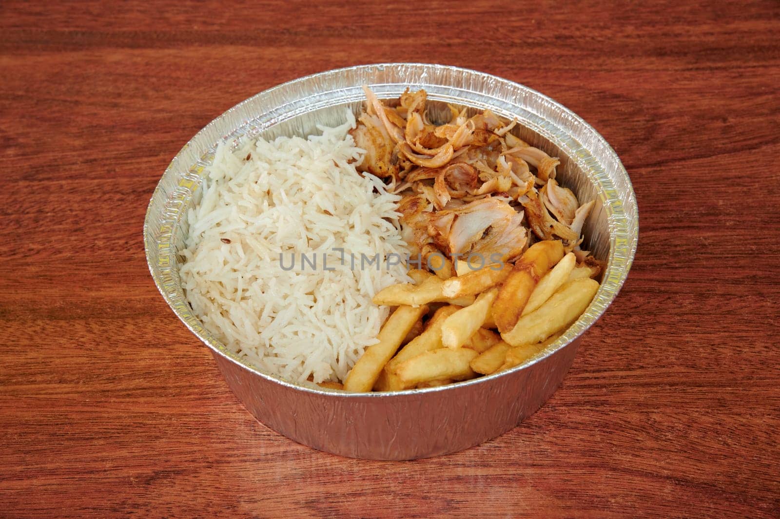 A bowl of food with rice, chicken, and french fries. The bowl is made of plastic and is sitting on a wooden table