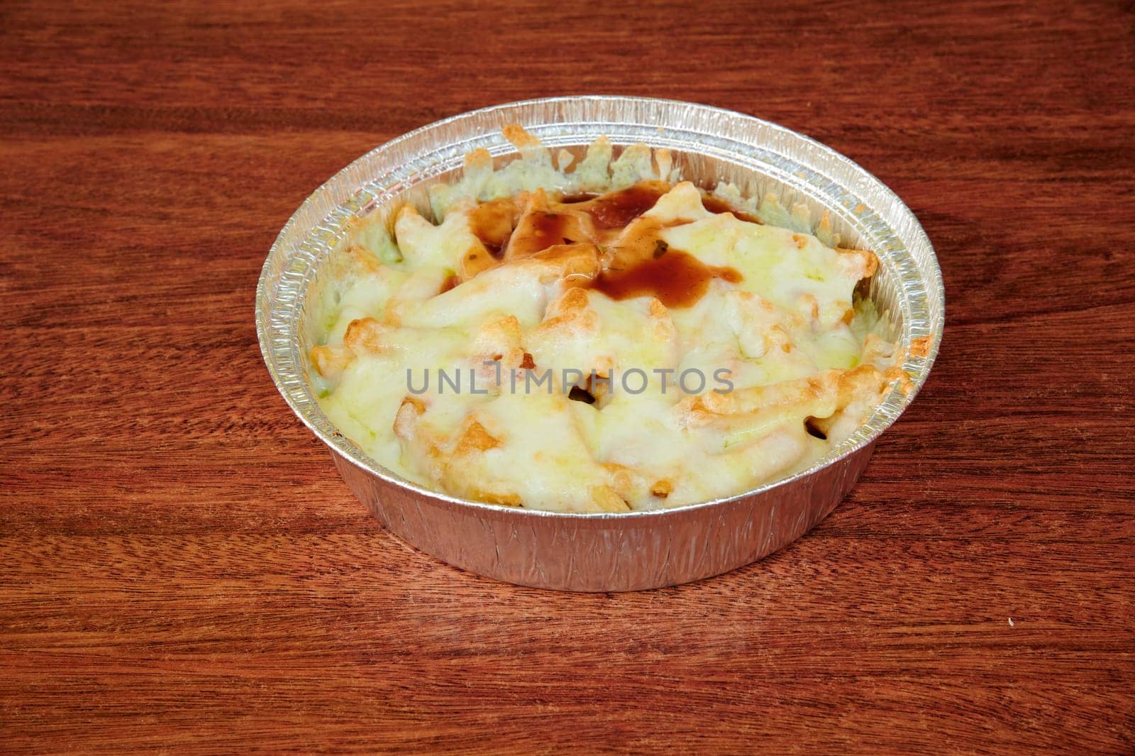 A bowl of pasta with cheese and sauce sits on a wooden table. The dish is covered in foil and he is ready to be eaten