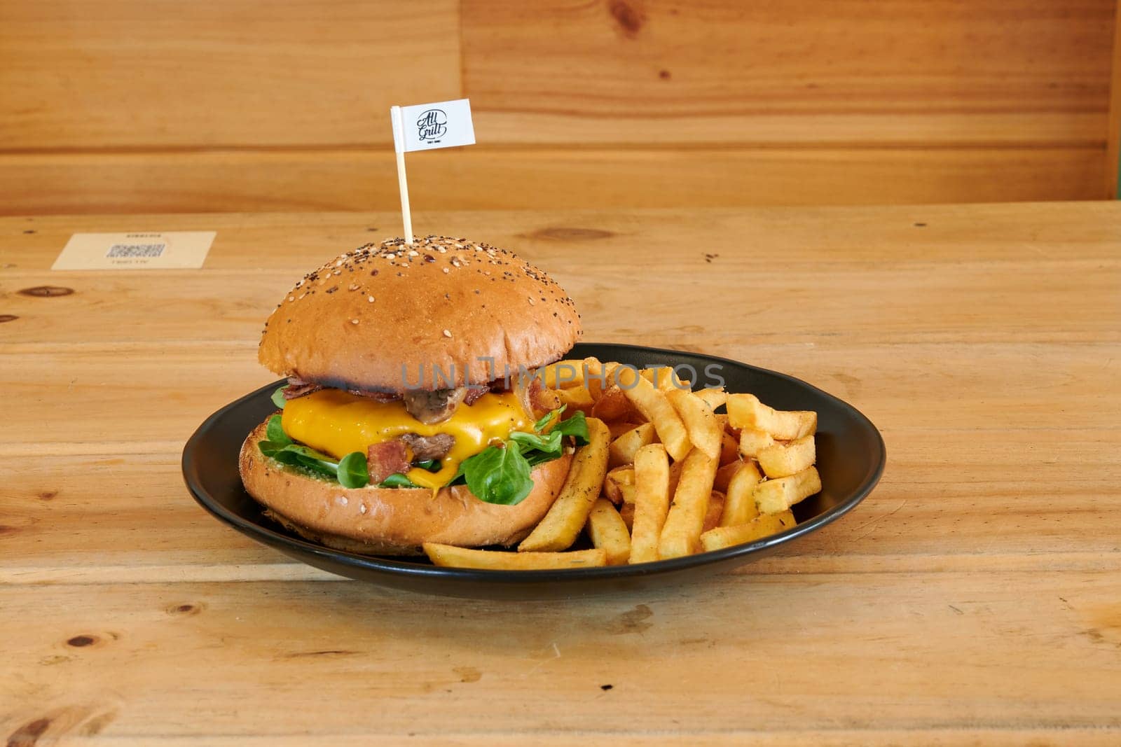 A burger with a flag on it sits on a plate next to a side of fries. The burger is topped with cheese and bacon, and the fries are golden and crispy. Concept of indulgence and satisfaction