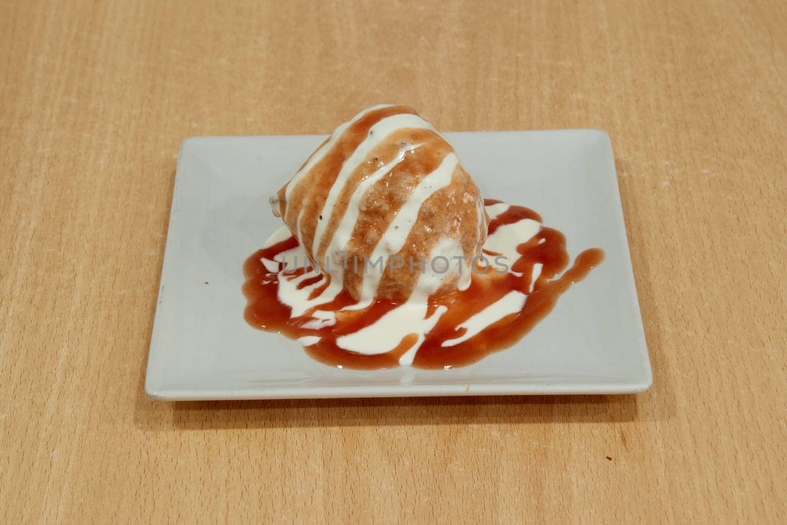 A dessert with a white and brown sauce drizzled on top is placed on a white plate. The dessert is a delicious treat that is perfect for satisfying one's sweet tooth. The combination of the white