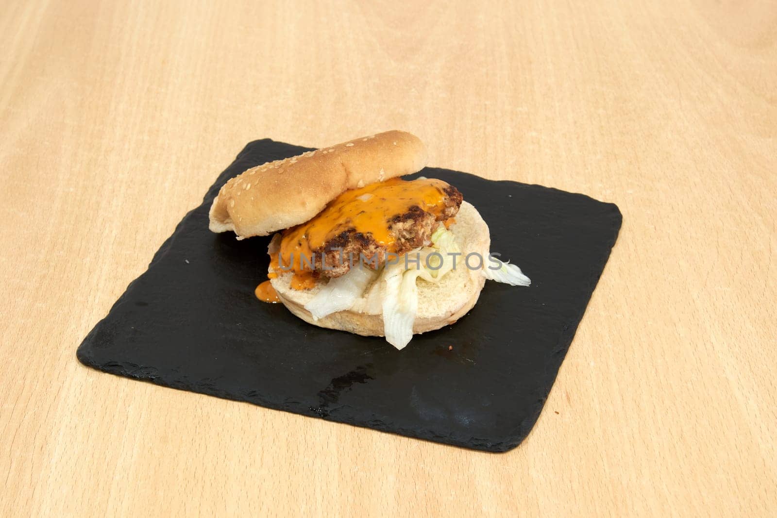 A burger with a slice of cheese on top of it. The burger is on a black plate