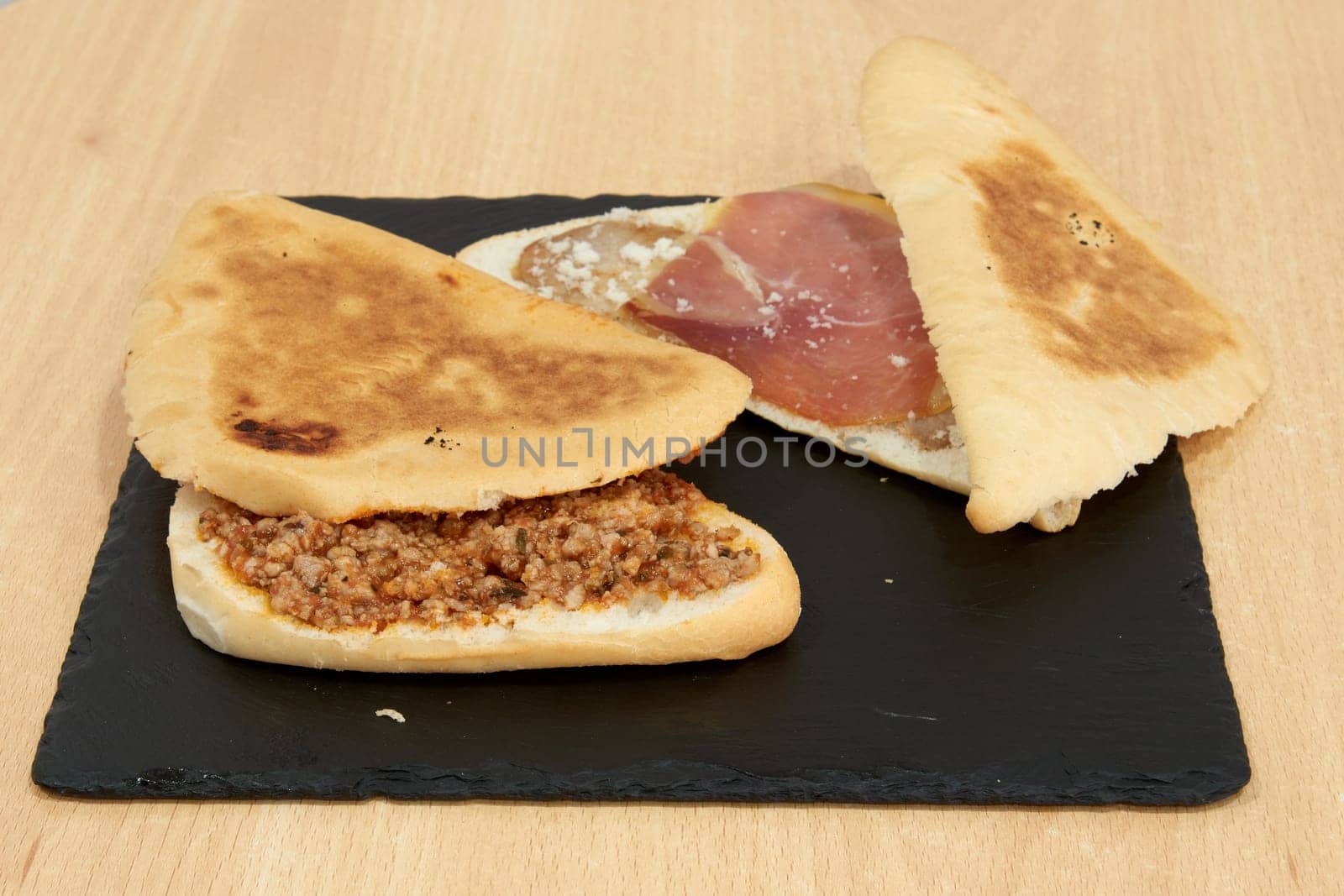 Three sandwiches are on a black table. One of the sandwiches is cut in half and has ham and cheese on it