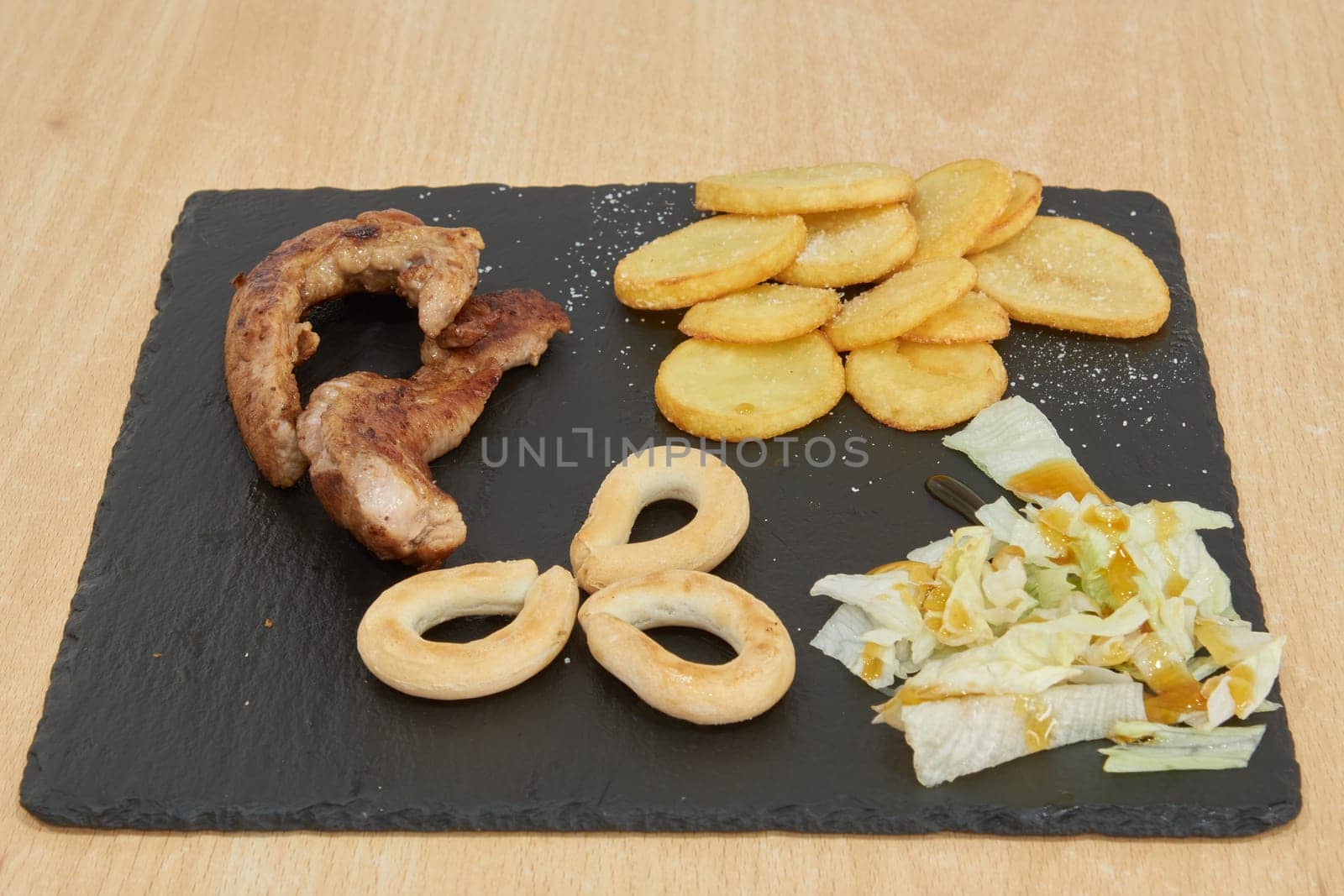 A plate of food with a variety of items including meat, potatoes, and vegetables. The plate is on a wooden table