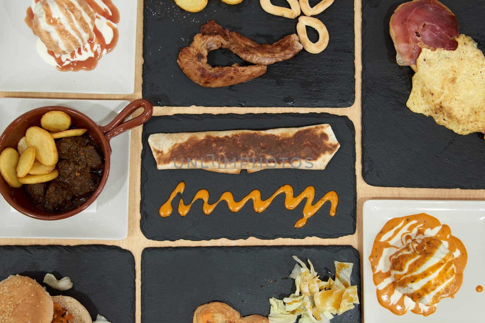 A variety of food items are displayed on a black table, including sandwiches, meat, and vegetables. The presentation is colorful and appetizing, with a mix of textures and flavors