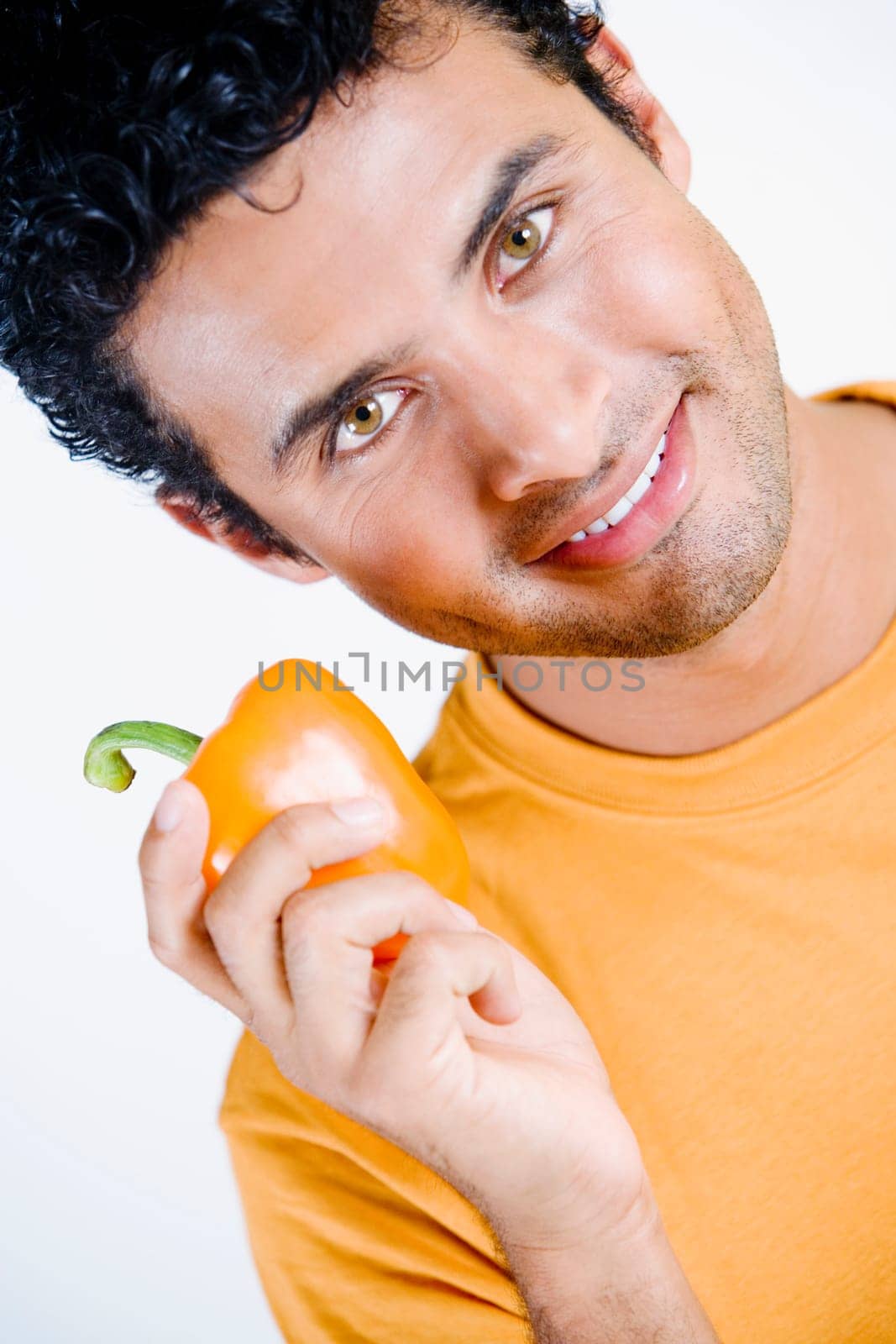 Portrait of a young man holding an orange bell pepper and smiling