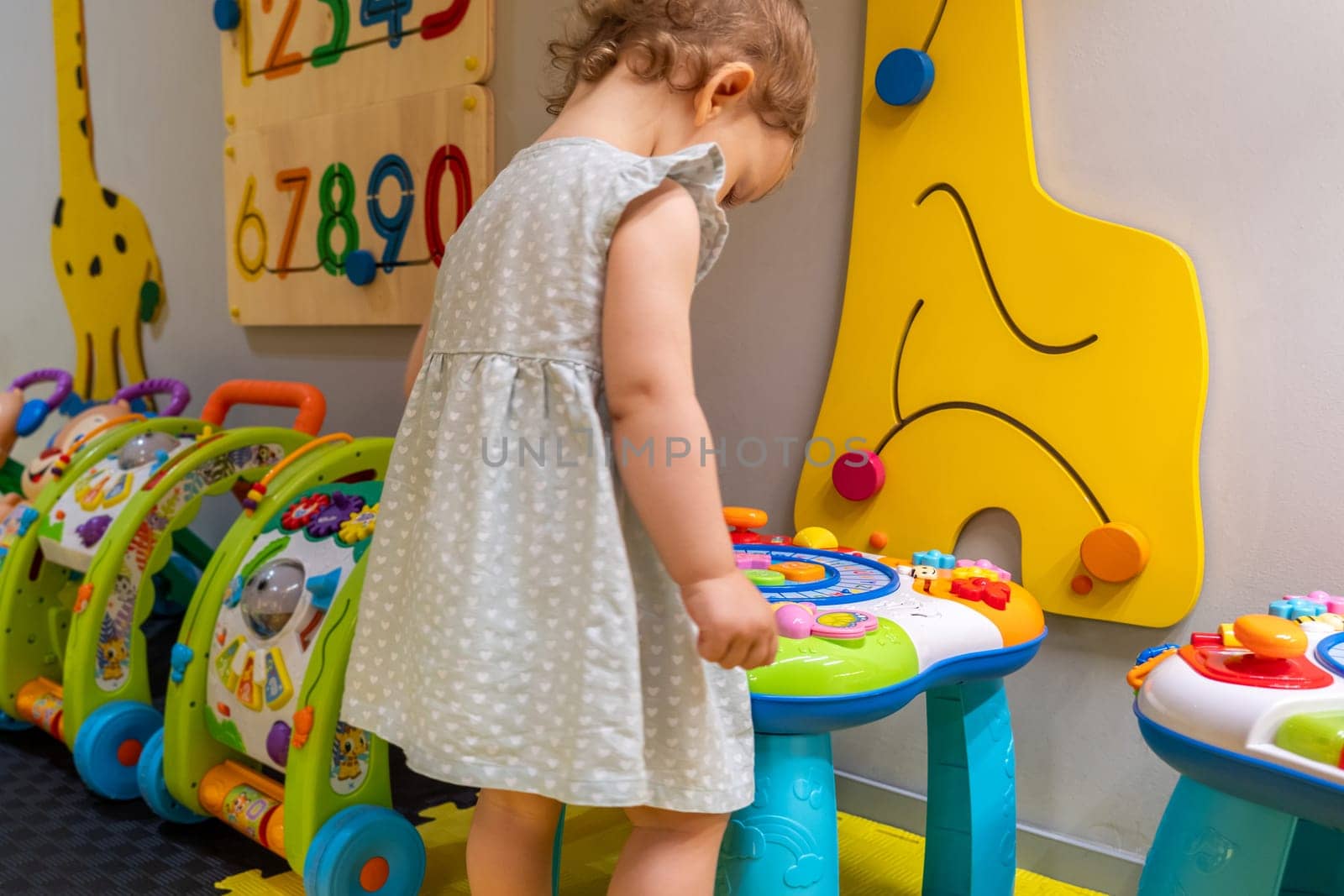 Child interacting with an educational activity table in a colorful playroom, developing motor skills and creativity. Concept of discovery and engaging early education through play