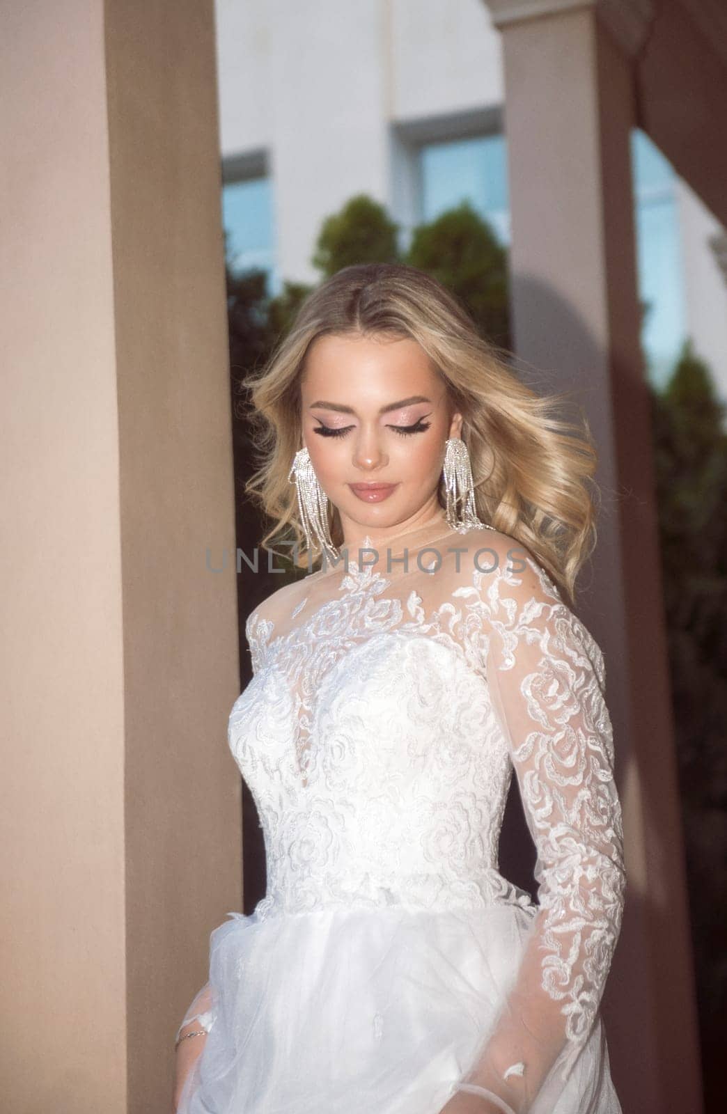 beautiful blonde bride walking along open gallery of hotel. in long wedding dress, with lace and chiffon corset. she has wavy blonde hair, beautiful earrings. she smiles