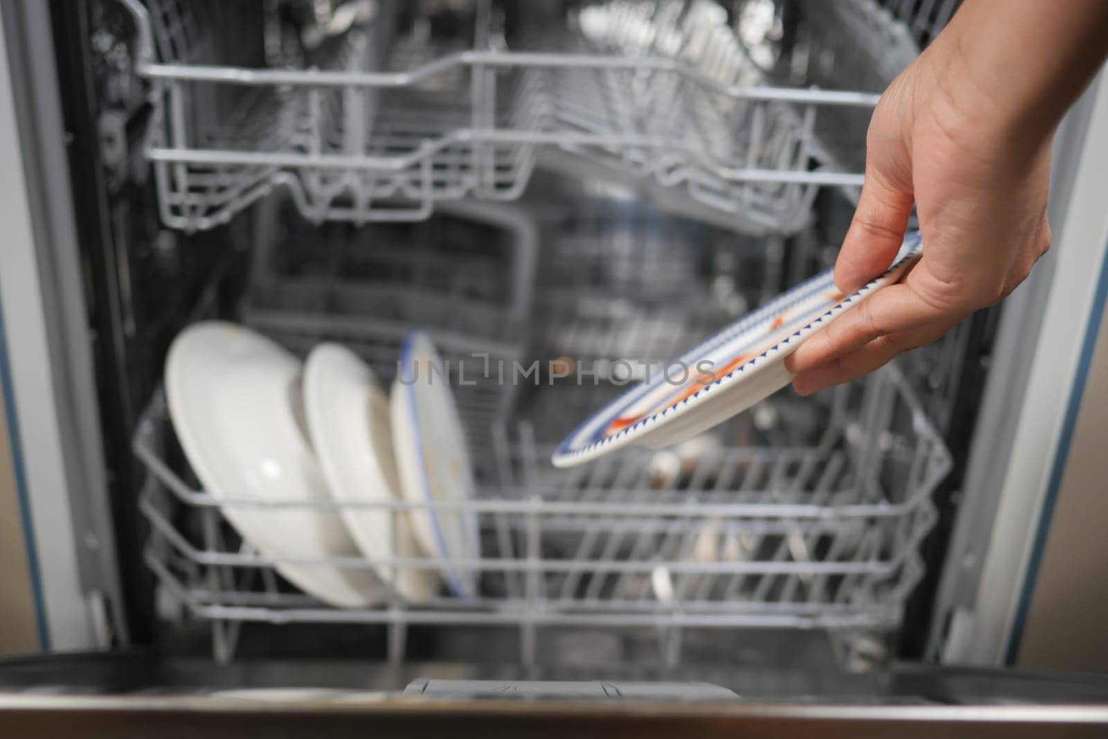 A person organizes clean plates inside a dishwasher after meals.