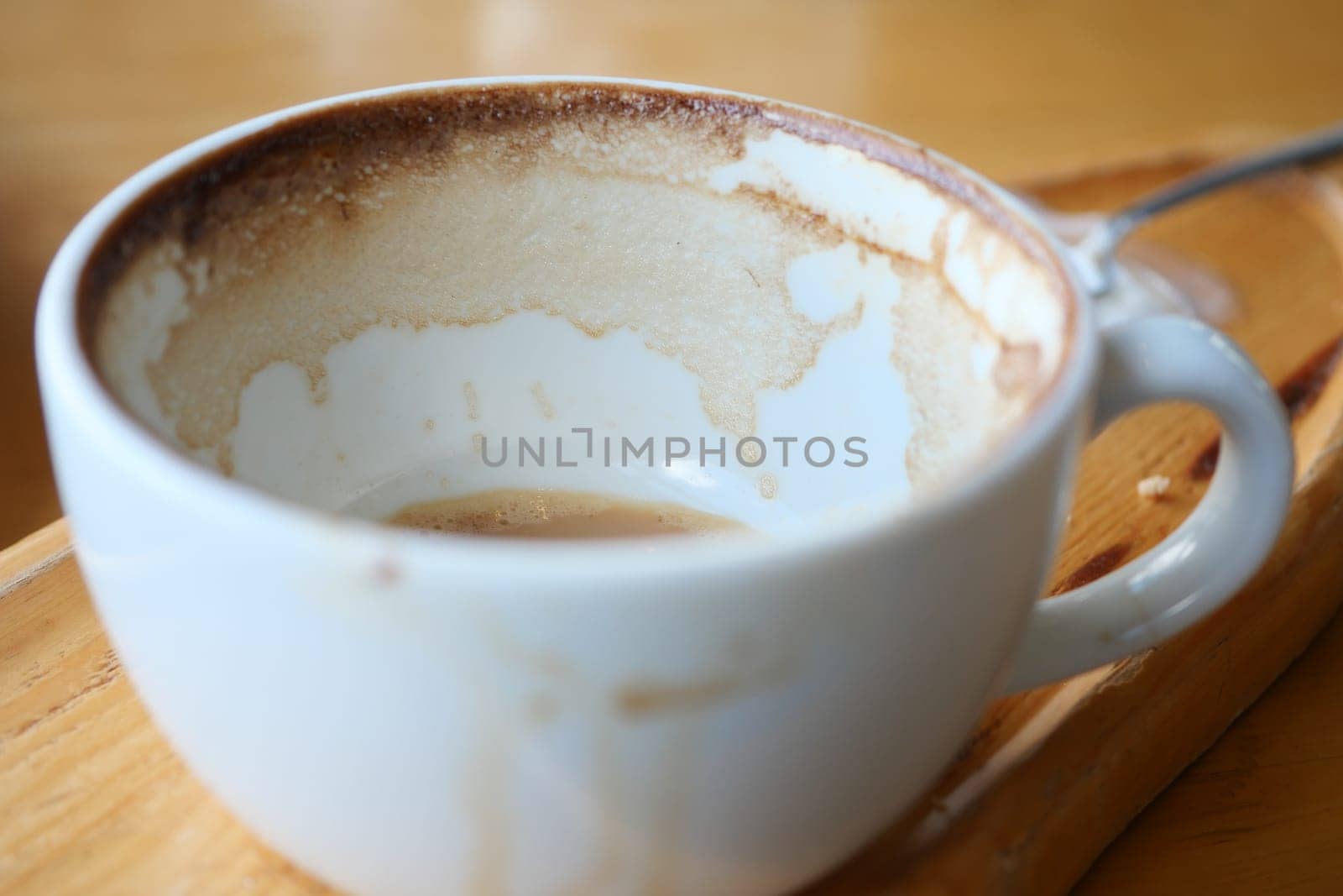 Cup sits empty on a wooden tray, showing the traces of a recent drink.