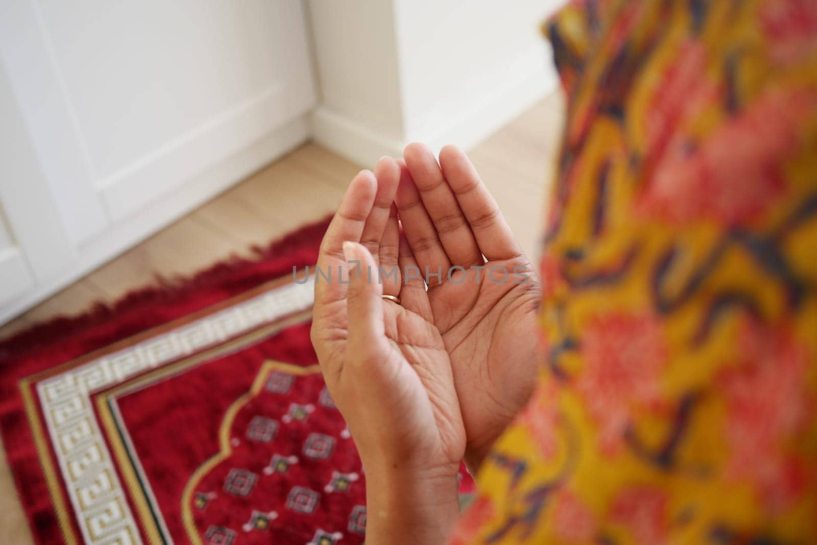 Hands are positioned for prayer on a vibrant rug in a peaceful space.