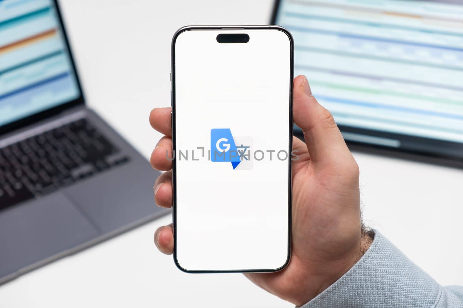 PRAGUE, CZECHIA - JULY, 2024: Google Translate logo on the screen of smartphone in mans hand and laptop on the background