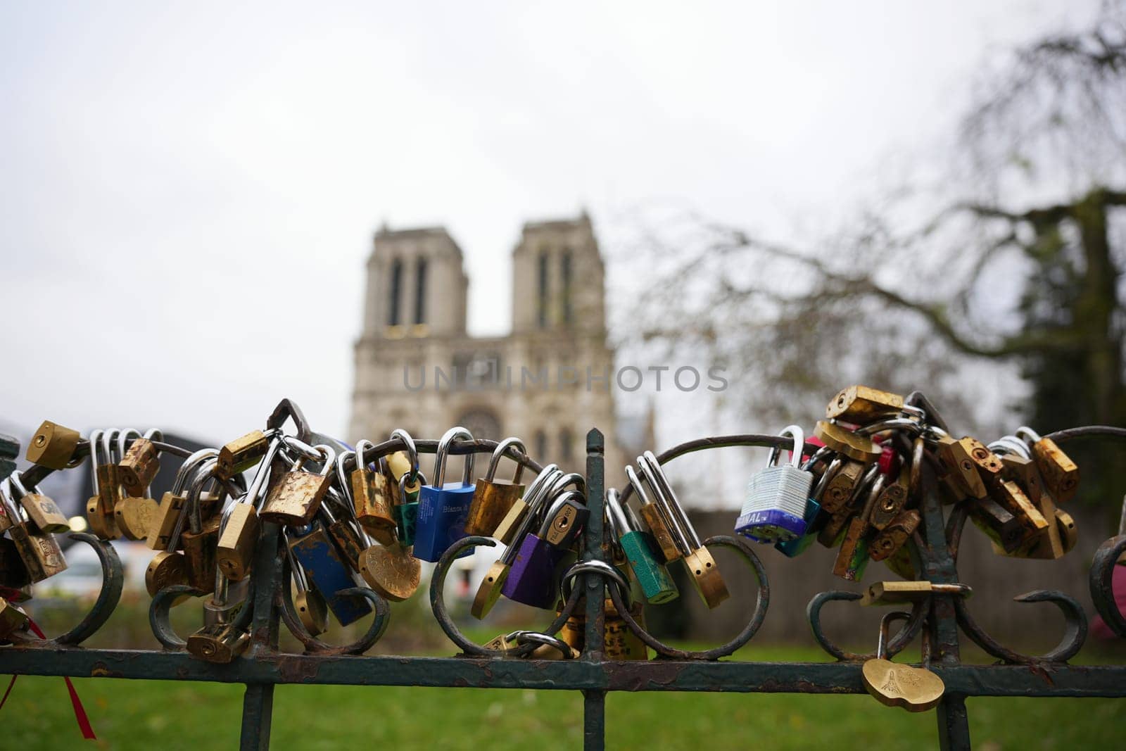 Close-up of colorful love locks attached to a fence in Paris, France 20.01.202, with the blurred towers of Notre Dame Cathedral in the background.
