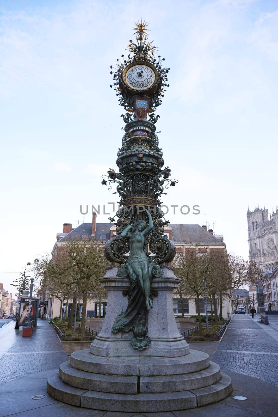 Detailed clock tower in Amiens. France 17.02.2025, featuring intricate bronze sculptures and a Gothic cathedral visible in the background.