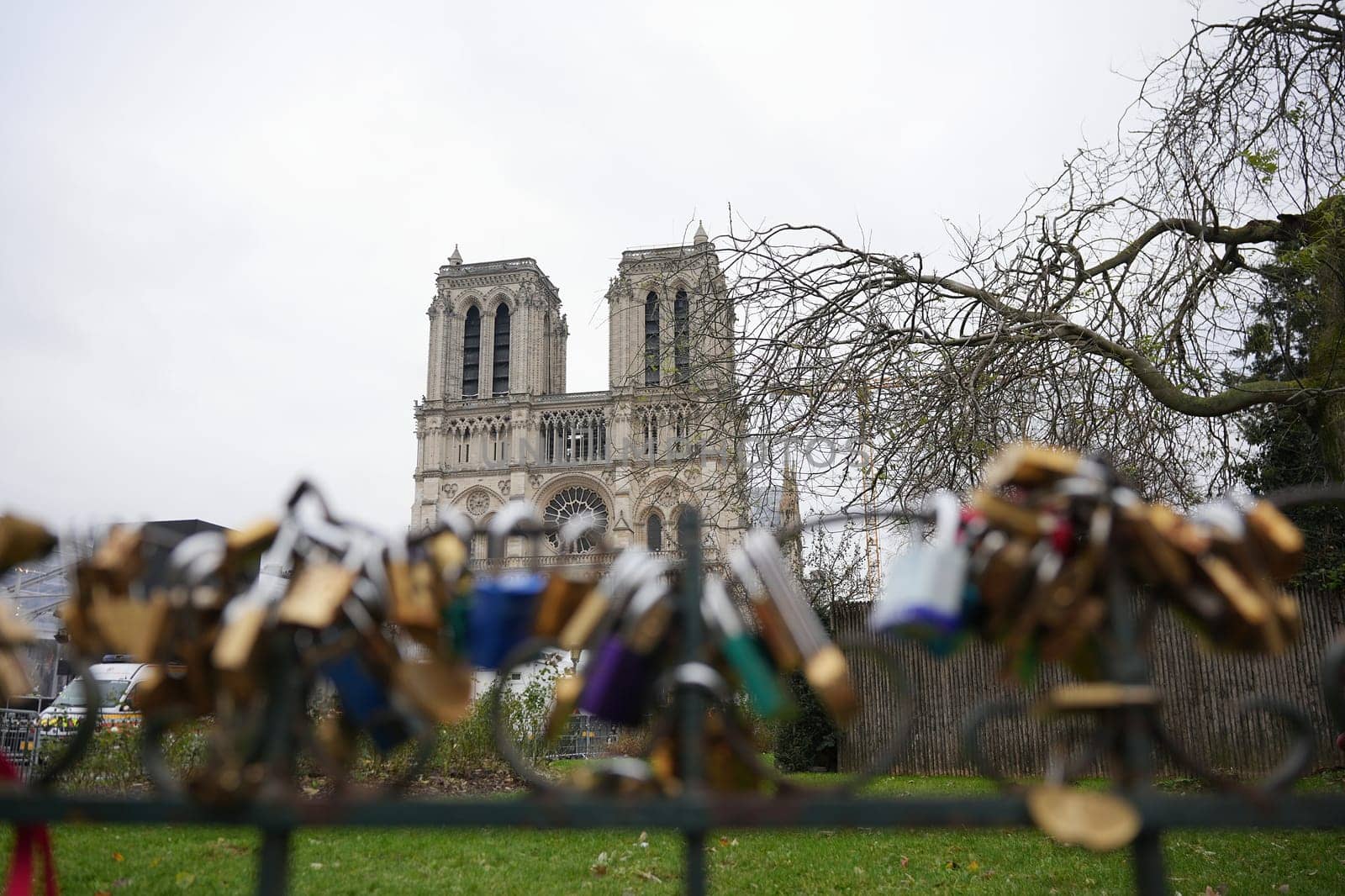 A picturesque view of Notre Dame Cathedral in Paris, framed by a foreground of love locks attached to a fence, under an overcast sky.