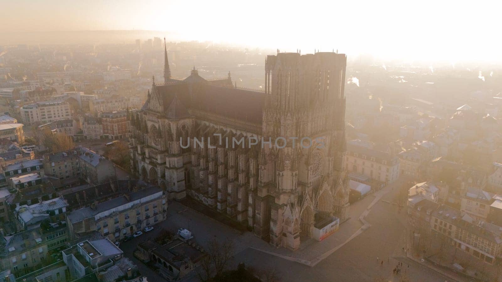 Aerial view of the Reims Cathedral in France during a golden sunrise. The Gothic masterpiece stands amidst the historic cityscape, exuding elegance and heritage.