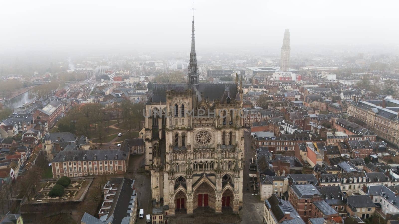 Aerial view of the Gothic Amiens Cathedral in northern France, surrounded by historic buildings and a foggy urban cityscape. A stunning UNESCO World Heritage landmark