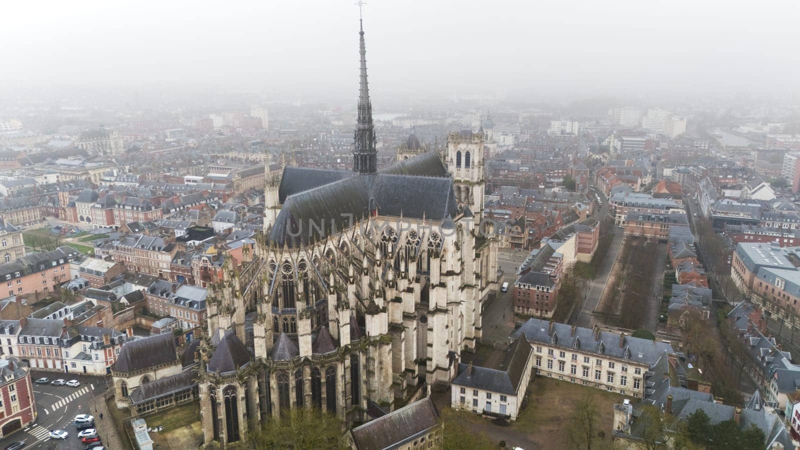 Aerial view of the Amiens Gothic Cathedral in France, showcasing its intricate architecture surrounded by the city's foggy urban landscape