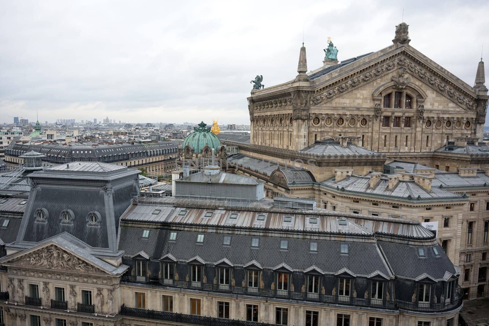 A captivating view of Parisian rooftops featuring the intricate details of Opera Garnier's facade and its gilded dome under a cloudy sky.
