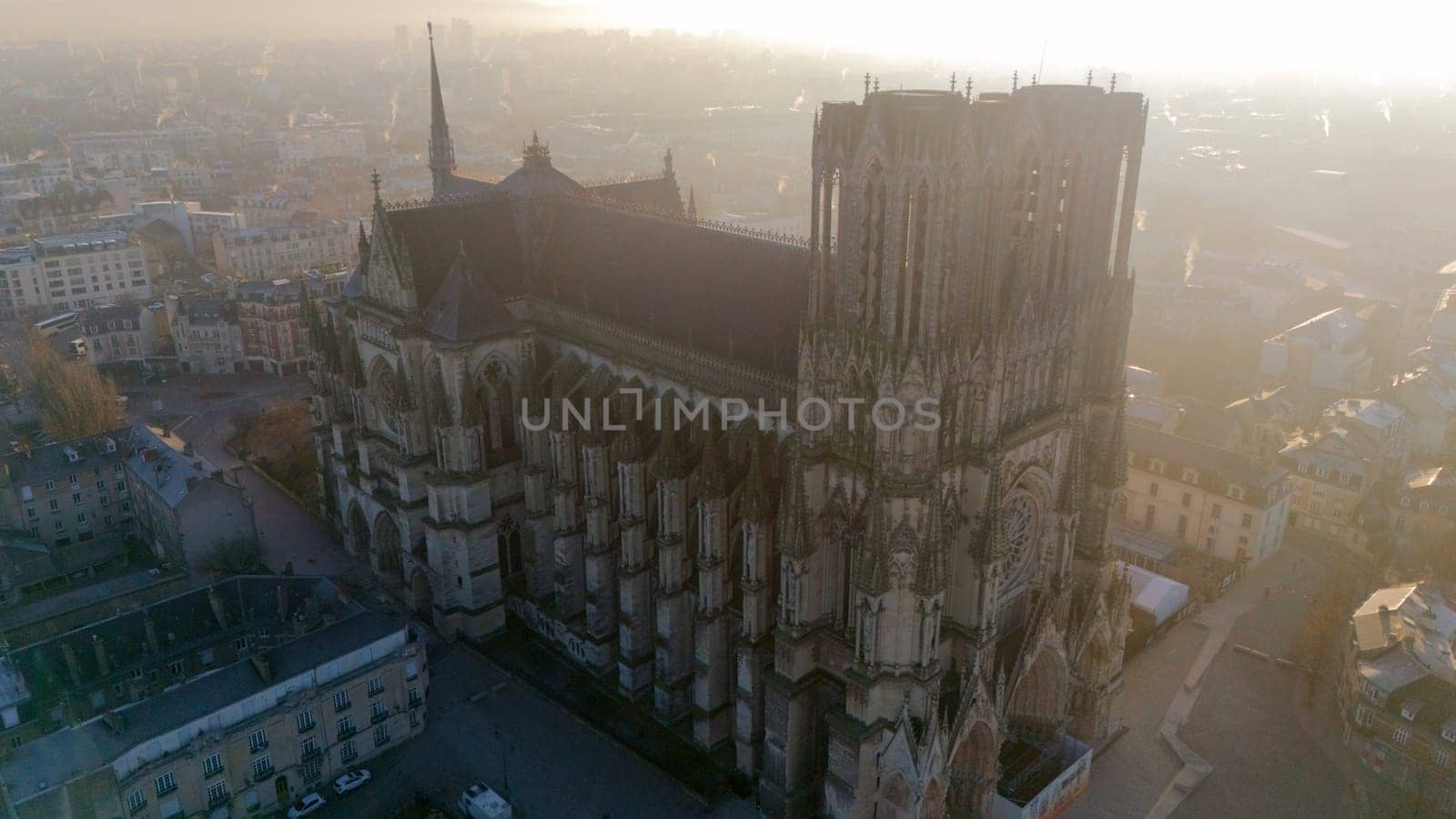 Aerial view of Reims Cathedral in France, glowing in soft golden morning light. This Gothic masterpiece is surrounded by the charming historic cityscape of Reims.