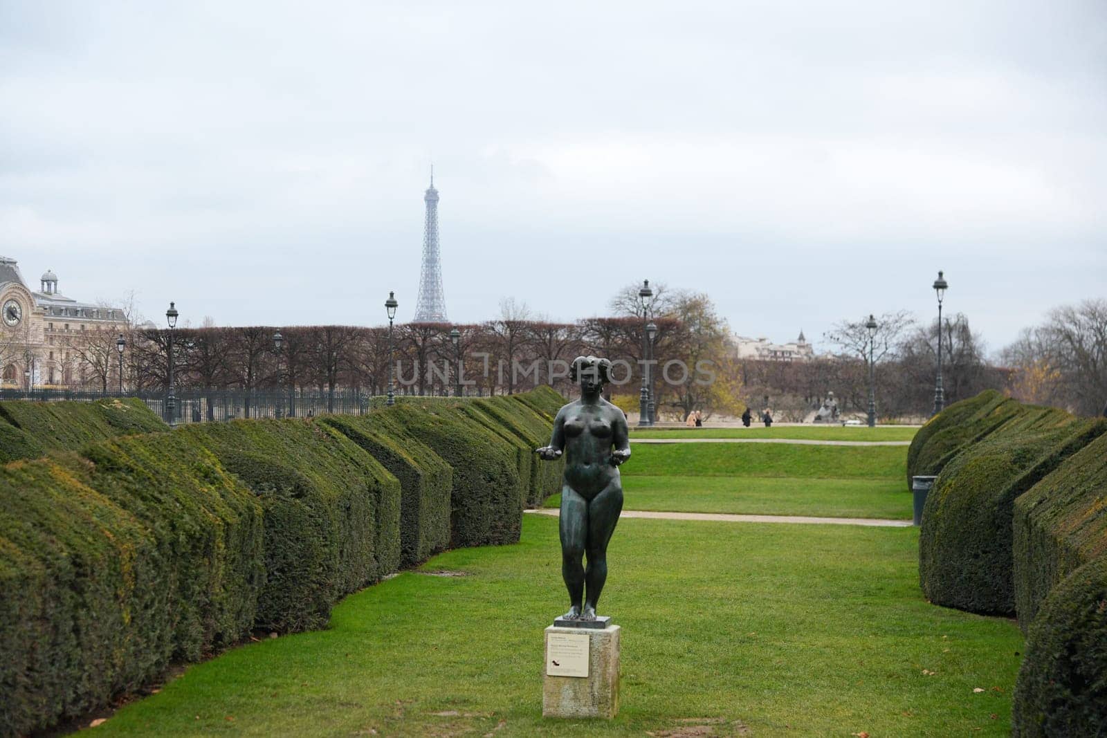 A serene view of the Tuileries Garden featuring a bronze statue, neatly trimmed hedges, and the Eiffel Tower under overcast skies. Paris, France 20.01.202