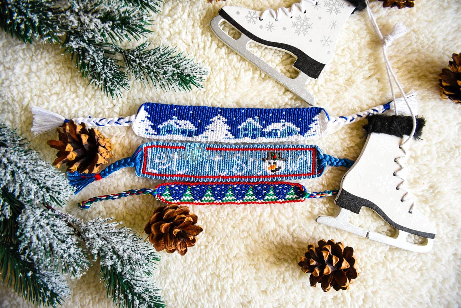 Woven friendship bracelets with alpha patterns Snowy night with houses and Let it snow. Handmade of thread, on  background with spruce cones,