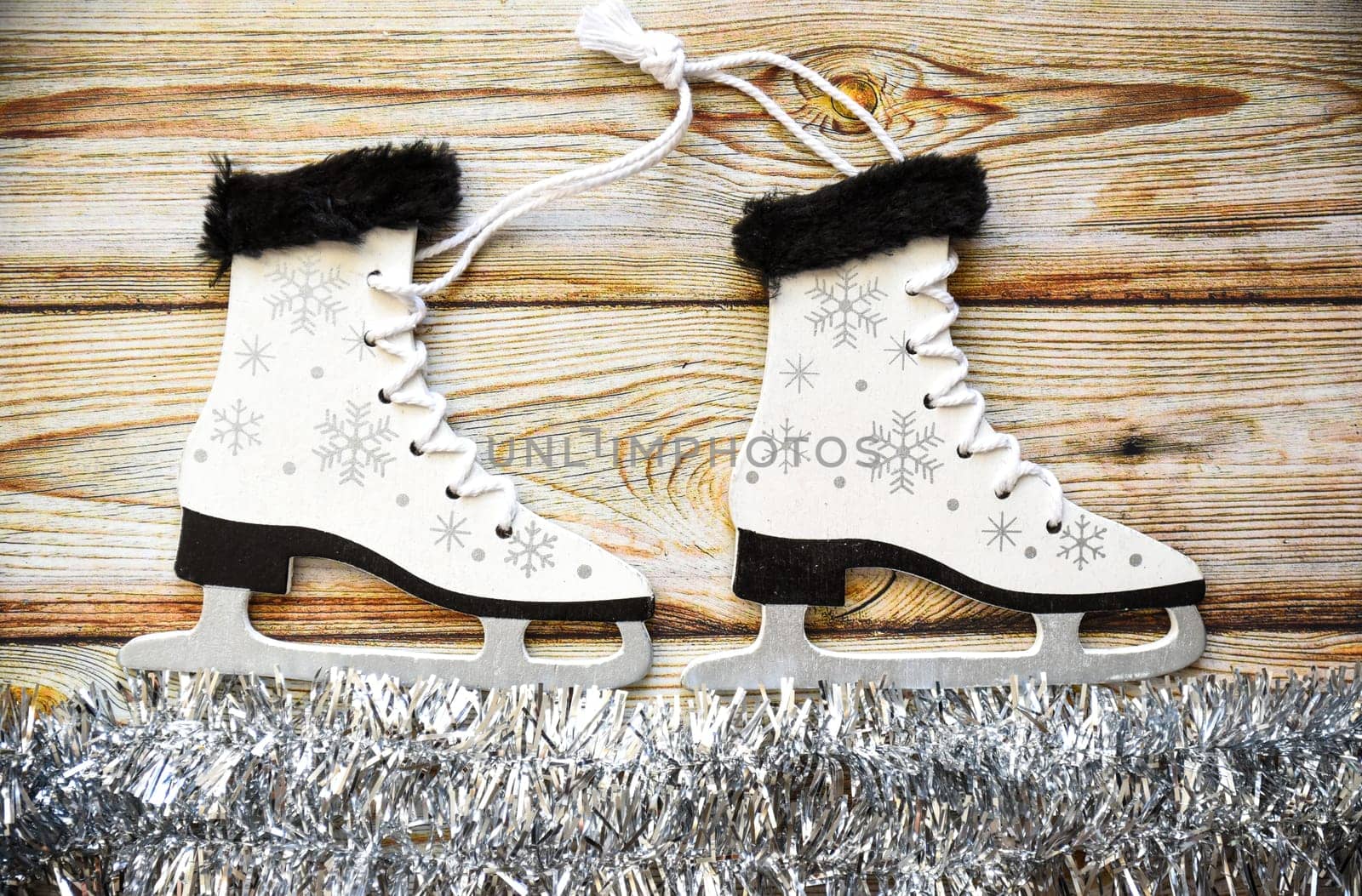Wooden Christmas tree toy Skates with snowflakes, tied with rope, on white tinsel imitating ice. Wooden background. Creative  New Year composition.