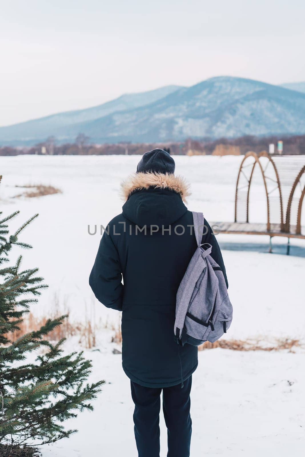 Young man solo traveler standing alone with backpack on winter background.