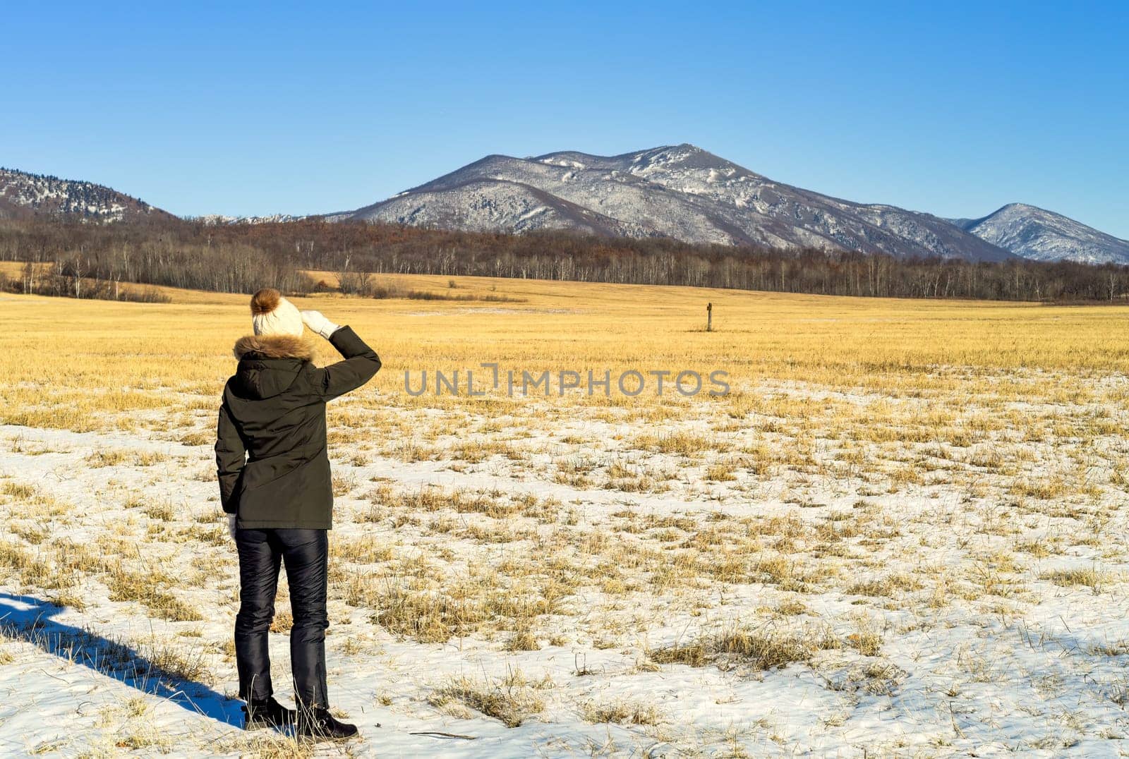 Young woman in warm clothes standing in the field and looking at snowy mountains. winter, Russia.