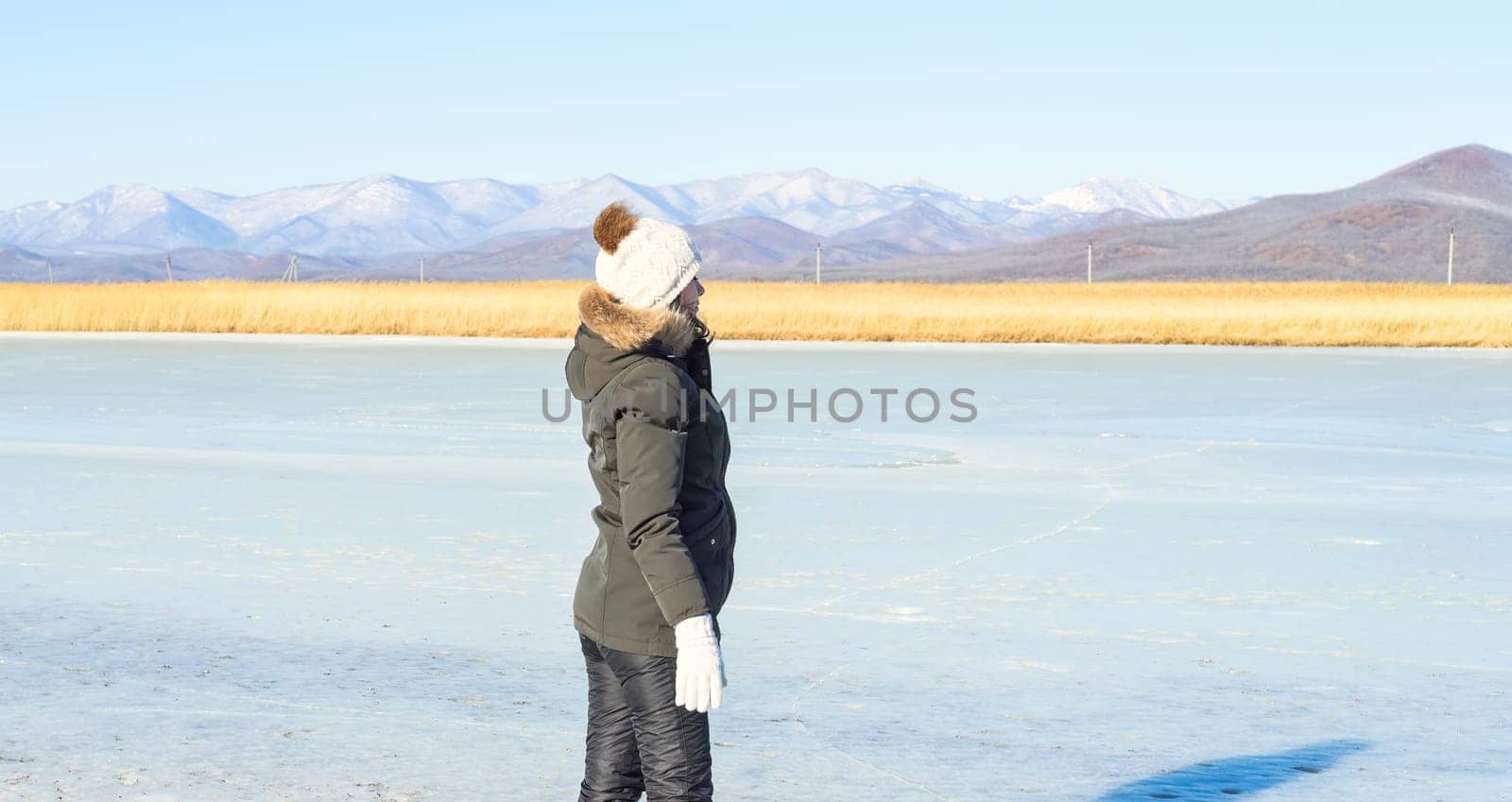 Young woman in warm clothes standing on the ice and looking at snowy mountains. winter, Russia.