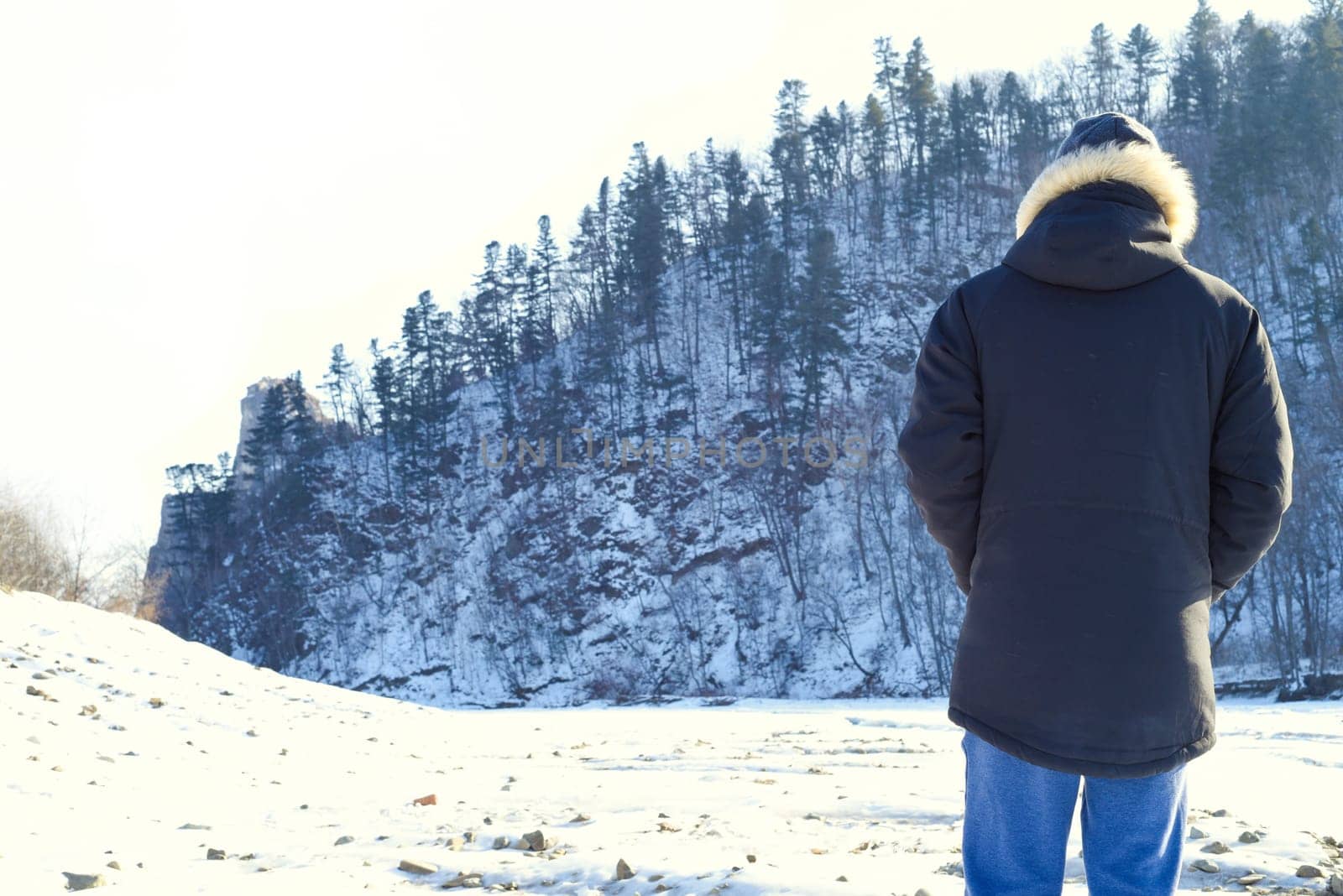 Man in warm clothes standing in the forest and looking at snowy mountains. winter, Russia.
