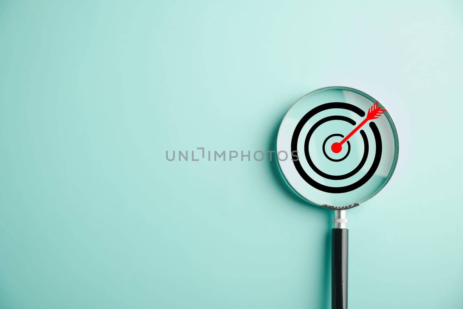 In this stock photo, a target board is magnified through a glass lens, symbolizing the business objective, target search concept, and achieving success. Isolated on a background with copy space.