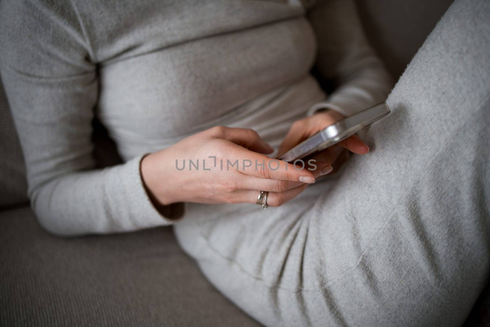 Caucasian female adult using smartphone in casual gray outfit at home.