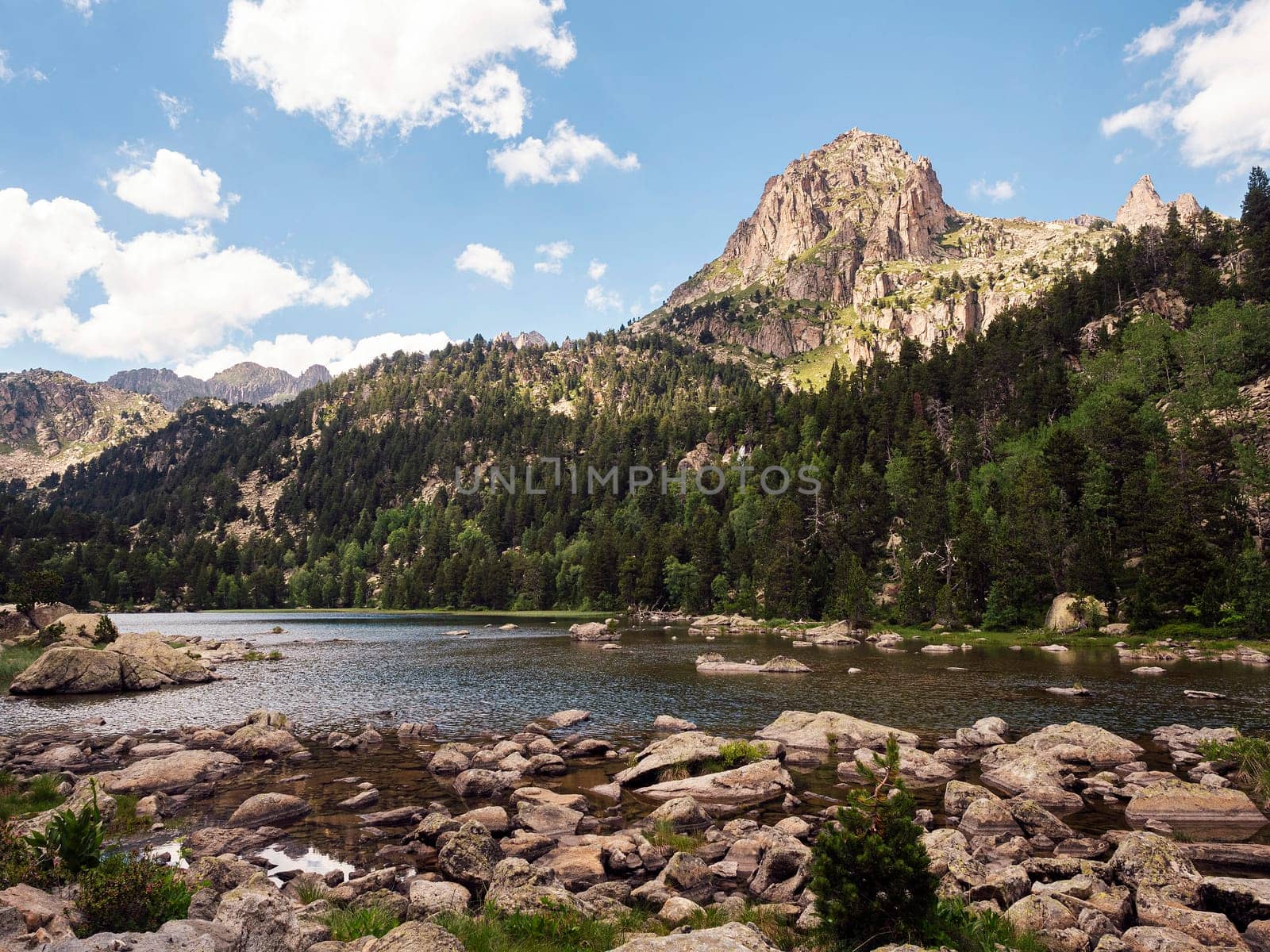 mountain range with a lake in the foreground the lake is surrounded by rocks and trees, the sky is clear and blue