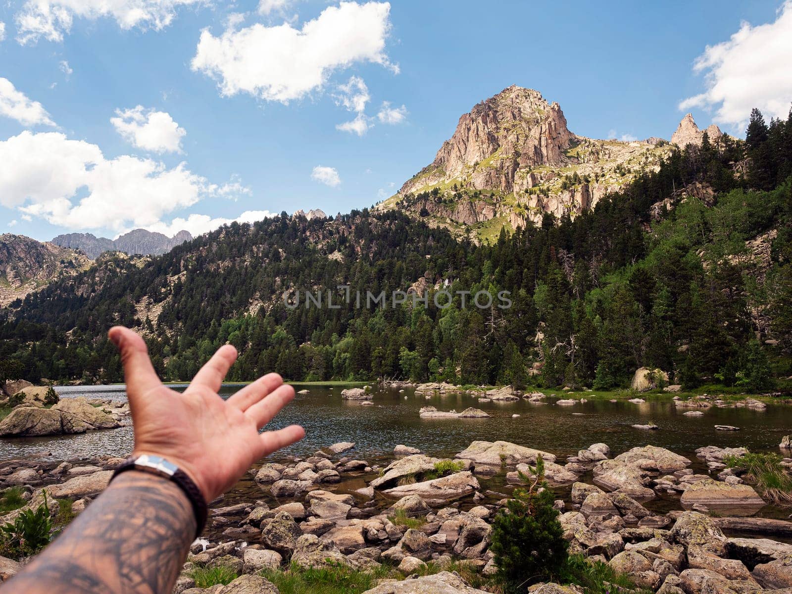 hand of unrecognizable traveler showing a mountain range, the scene is serene and peaceful, with a body of water in the foreground and a mountain range in the background