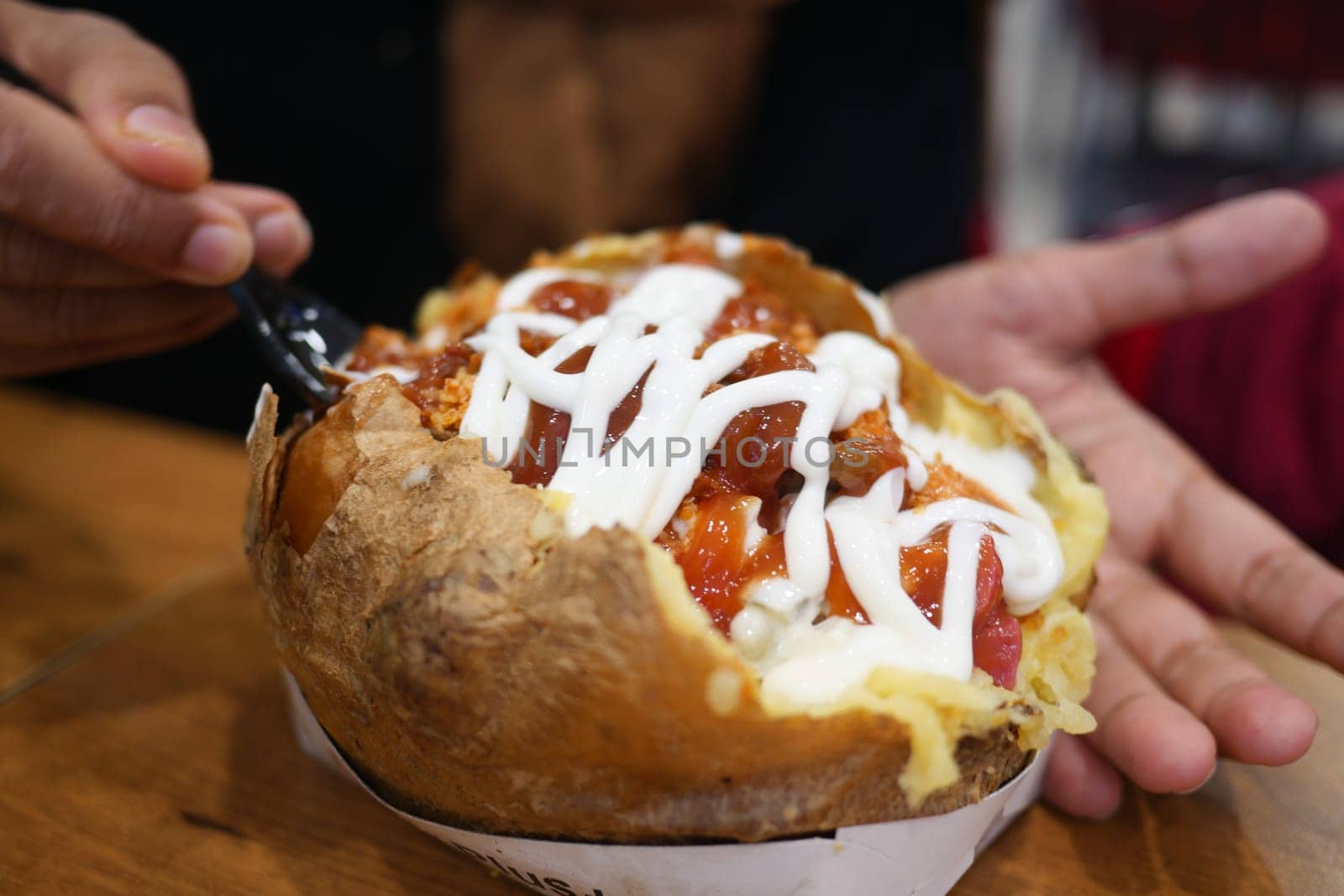 A person enjoys a loaded baked potato topped with toppings in a restaurant.