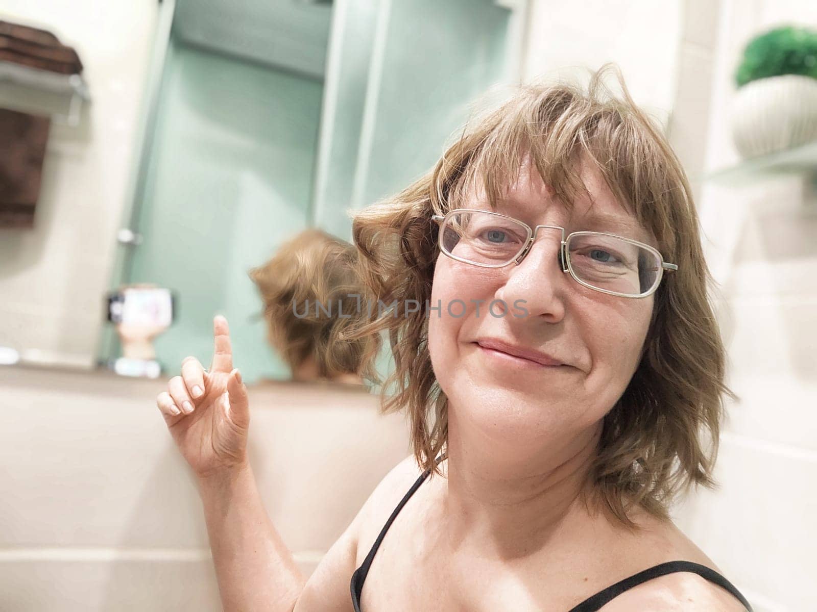 A middle-aged woman takes a morning selfie in her bathroom mirror, smiling and enjoying her blogging journey.