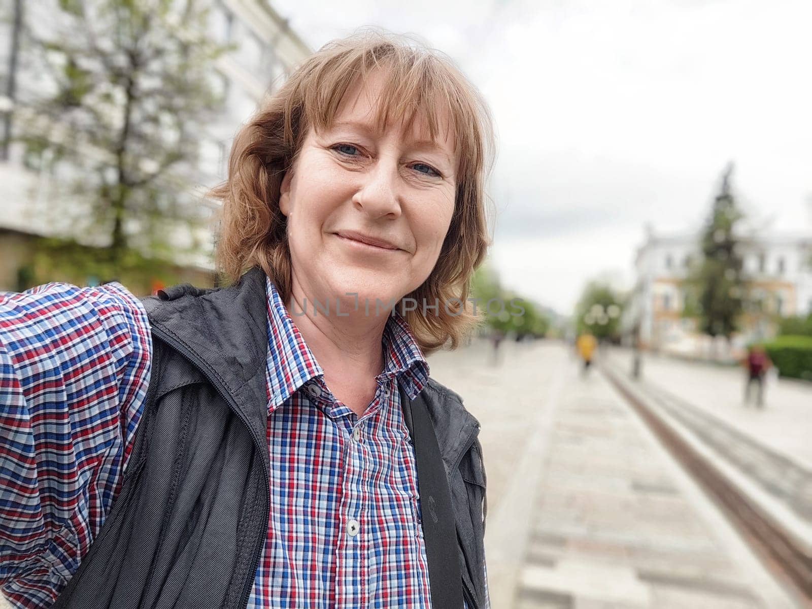 A middle-aged female traveler captures a cheerful selfie while exploring a lively cityscape on a beautiful day.
