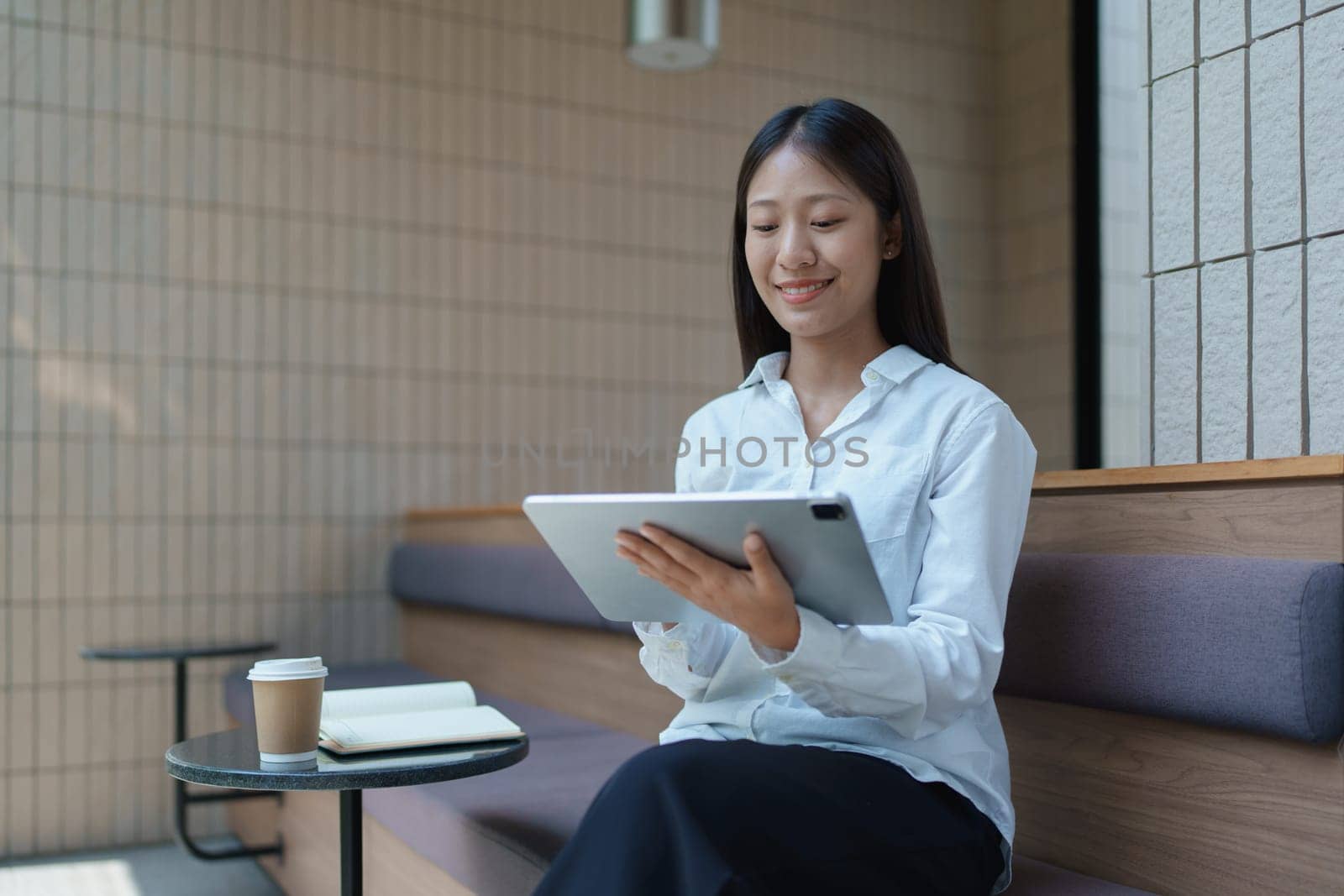 Young woman using tablet in modern coffee shop with notebook and coffee on a stylish table.