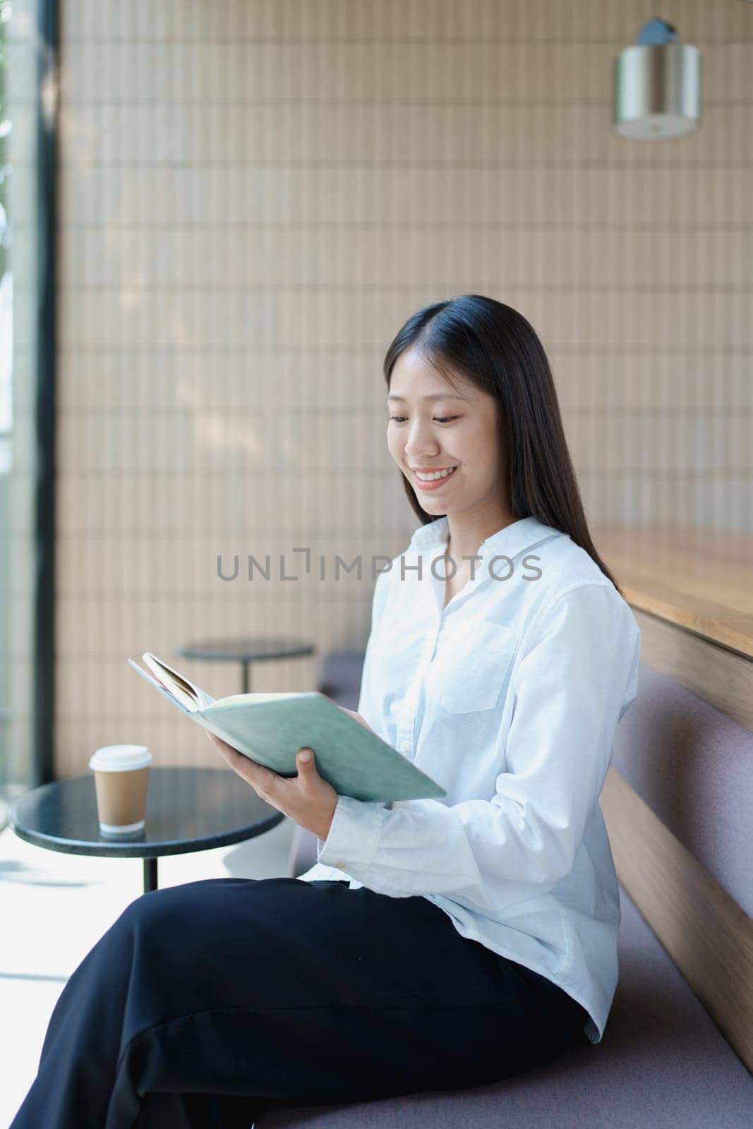 Young woman enjoying a peaceful moment reading a book in a modern coffee shop setting with natural light.