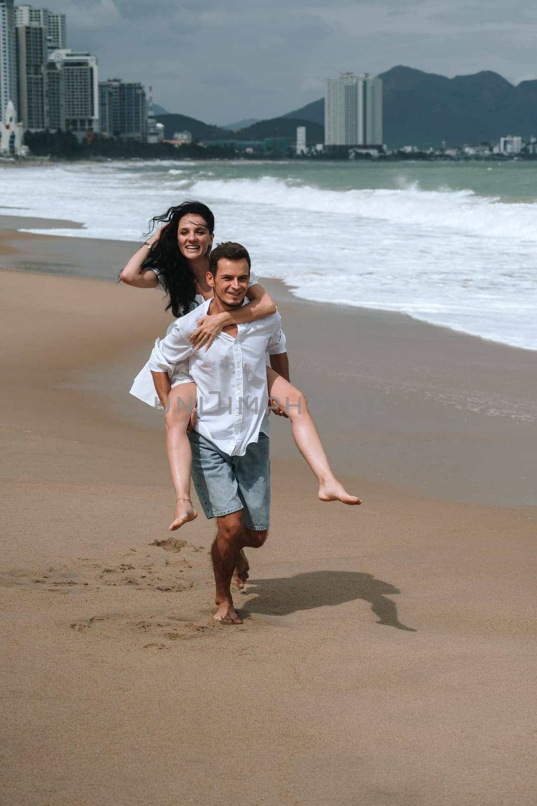 A beautiful young couple in love runs along the beach by the sea in summer. Piggyback ride