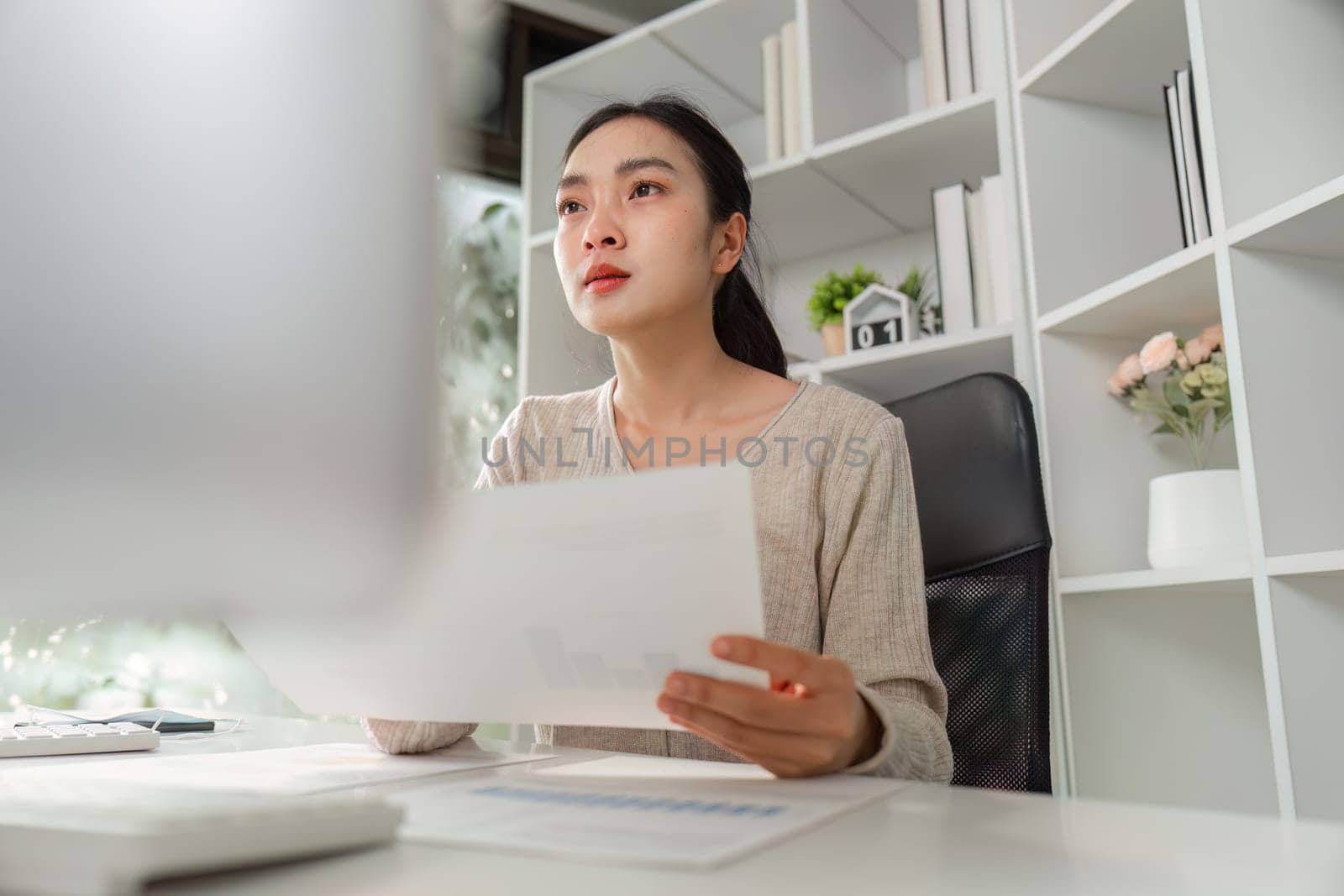 An office worker looks thoughtfully at financial reports, reflecting focus and the challenges of managing work-related stress.