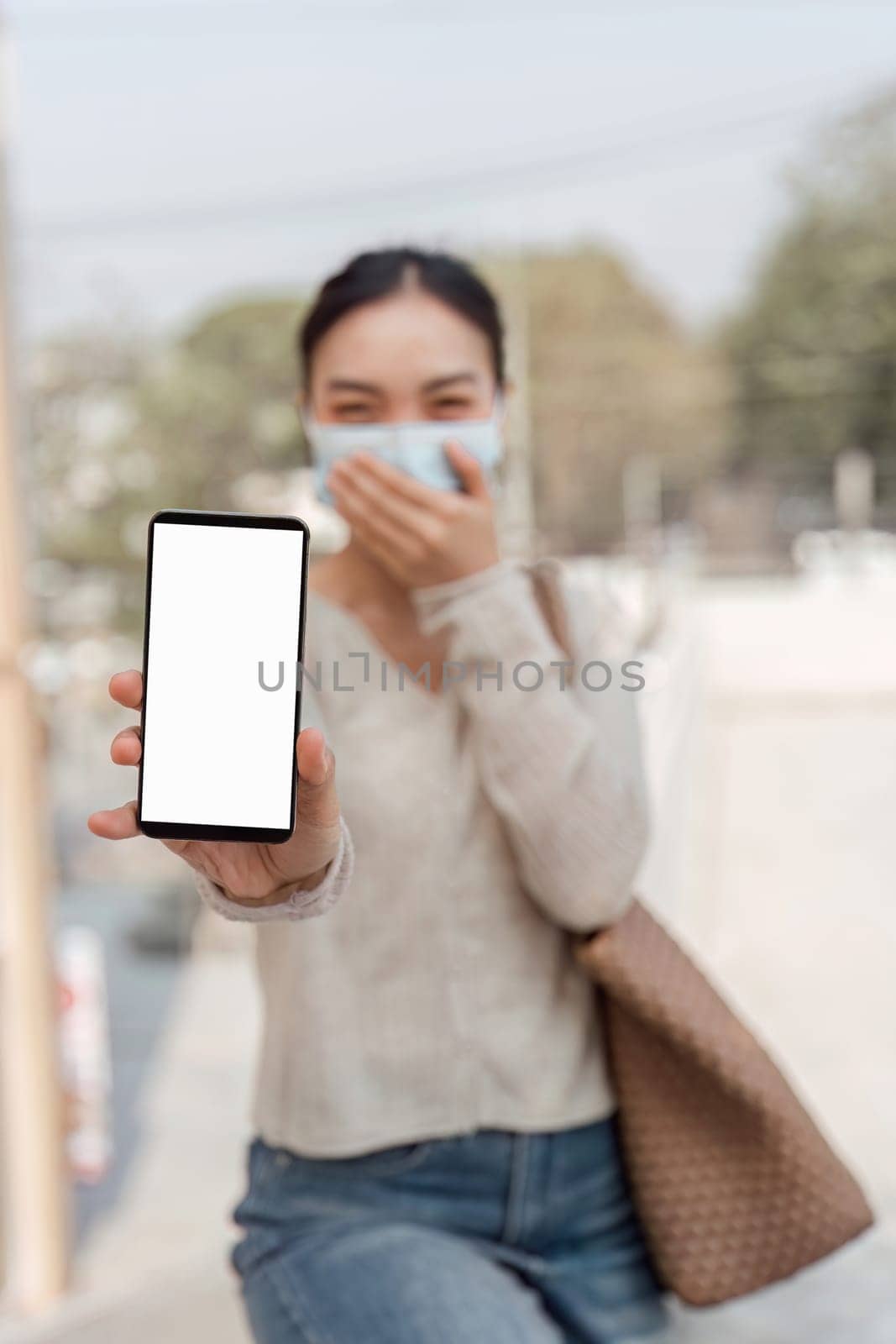 A young woman in a mask holds a smartphone while expressing discomfort, indicating health concerns related to pollution.