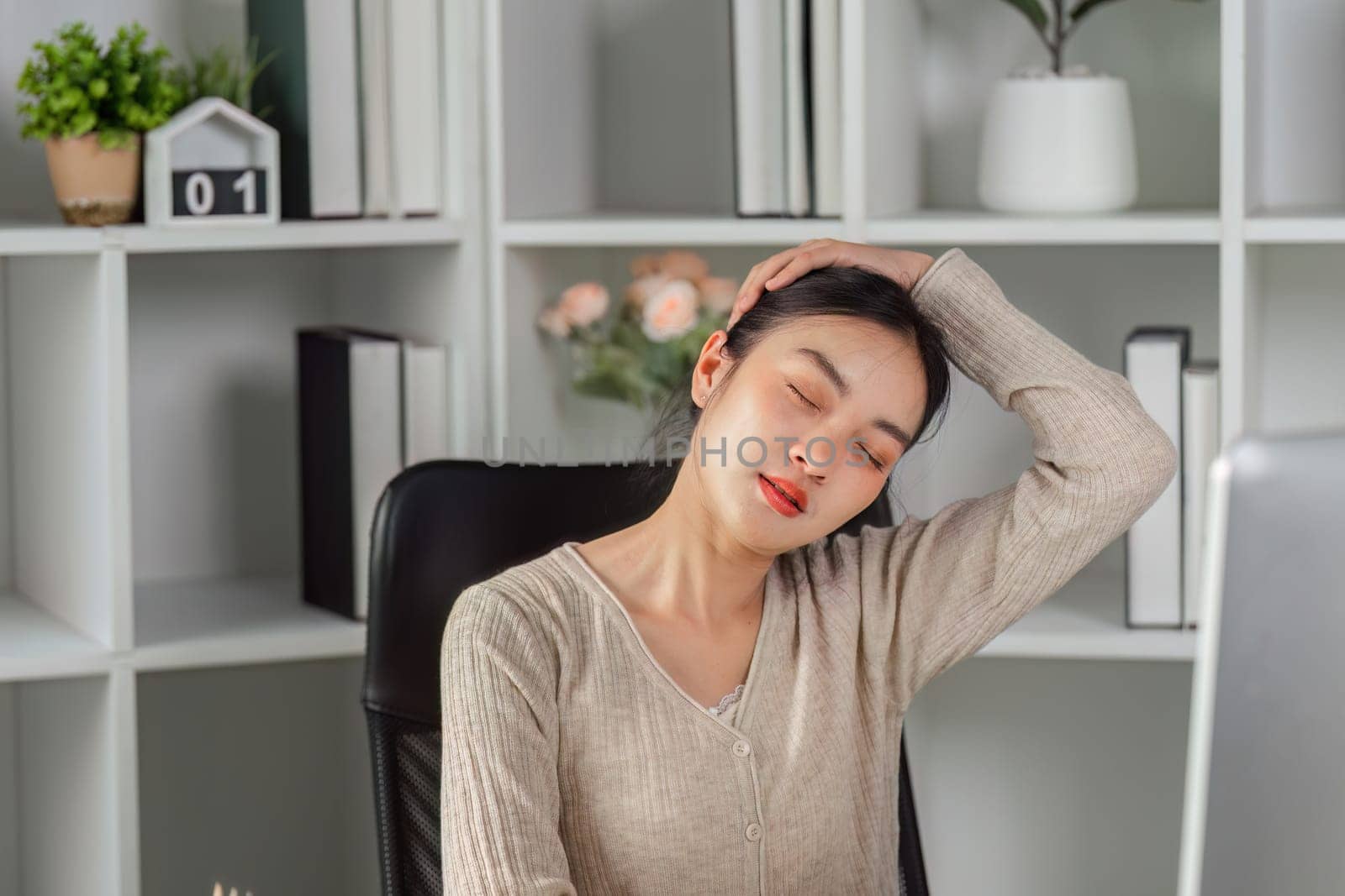 A young woman stretches her neck at her desk, relieving tension and promoting wellness in her modern office environment.