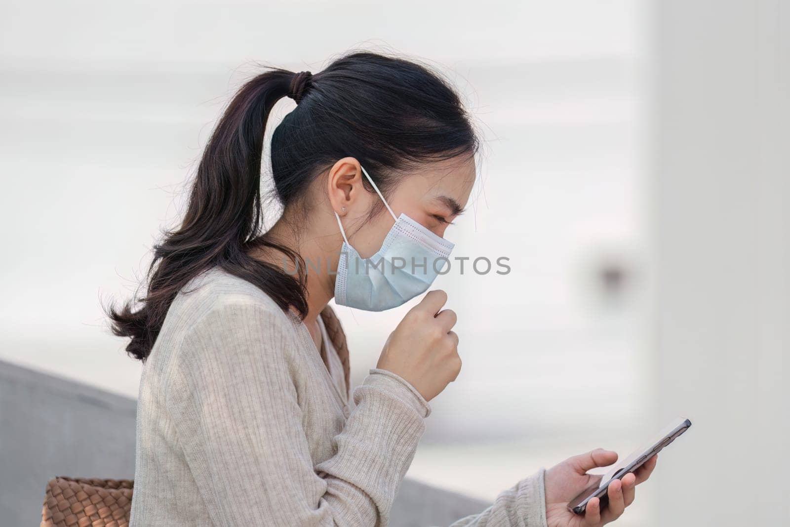 A young woman in a mask shows concern while checking her smartphone, illustrating the impact of pollution on daily life.