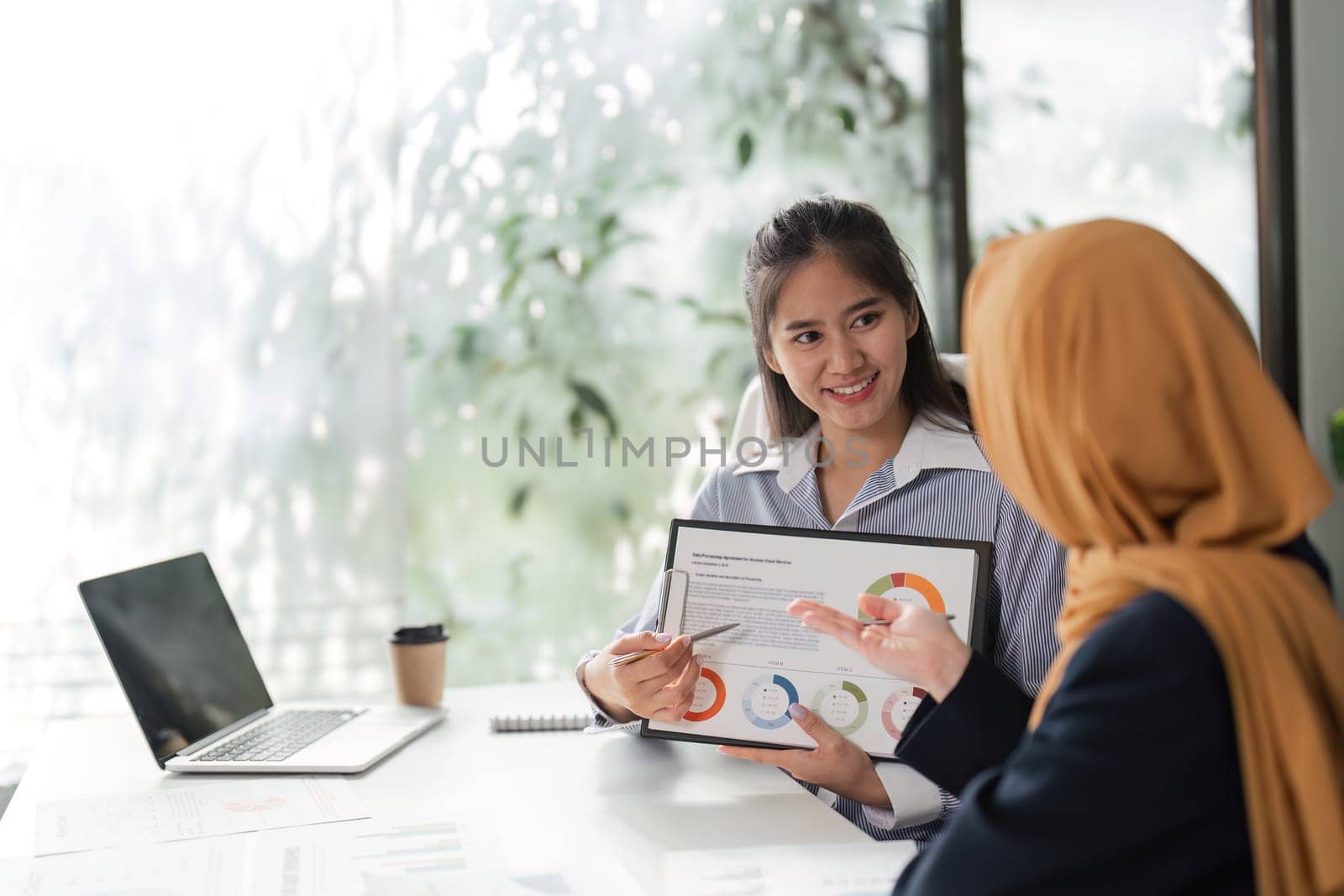 A woman presents financial data on a tablet while another listens, fostering collaboration in a professional setting.