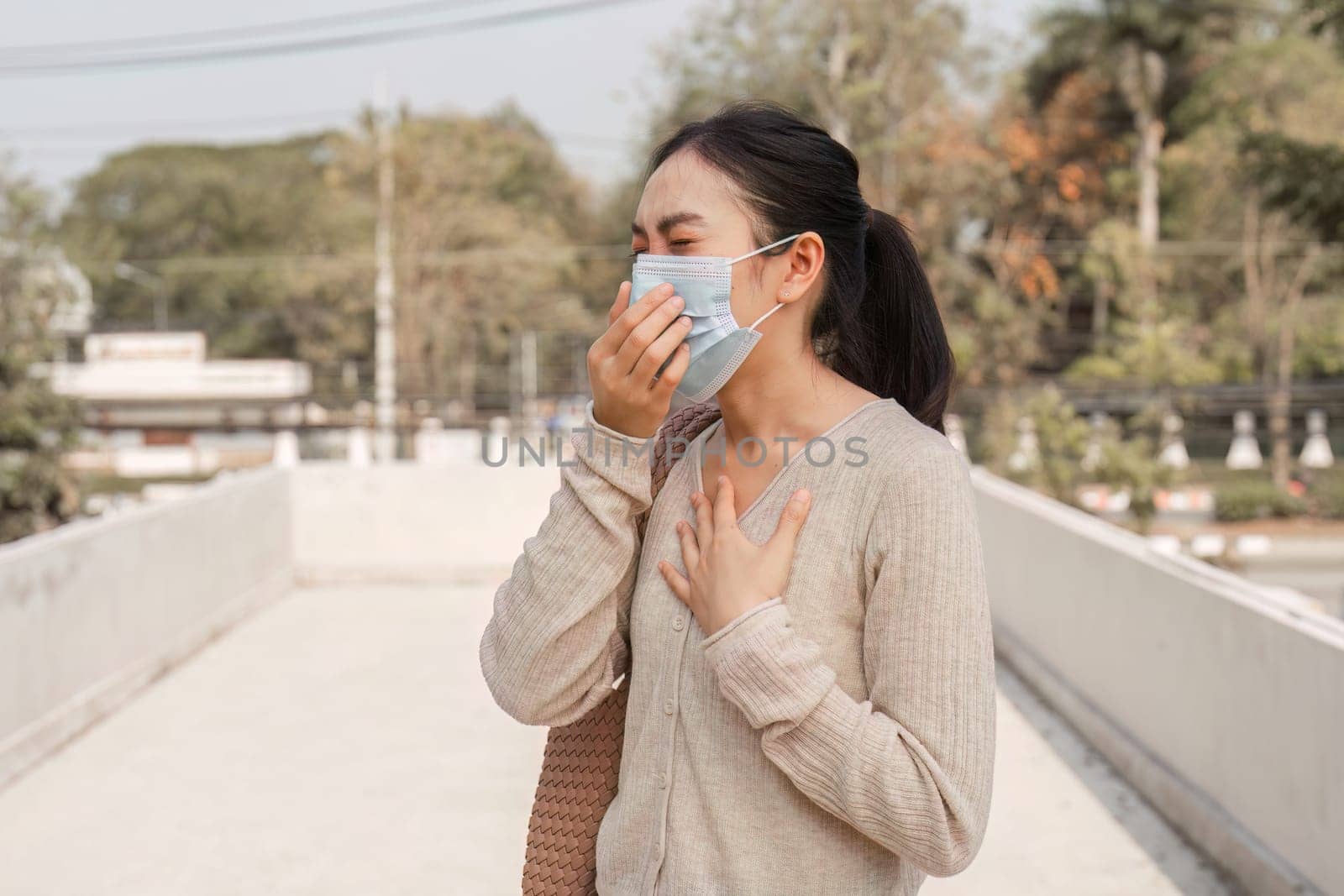 A woman wearing a mask expresses discomfort while standing outside, highlighting the impact of pollution on health.