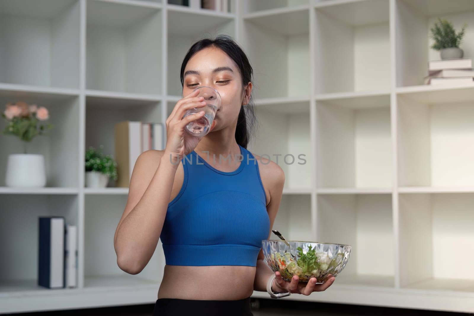 A young woman drinks water while holding a salad, focusing on healthy eating and weight management.